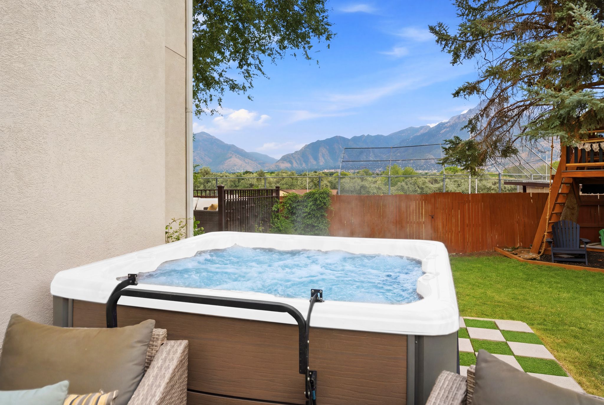 Outdoor spa with mountain backdrop, bordered by a textured exterior wall and a manicured lawn