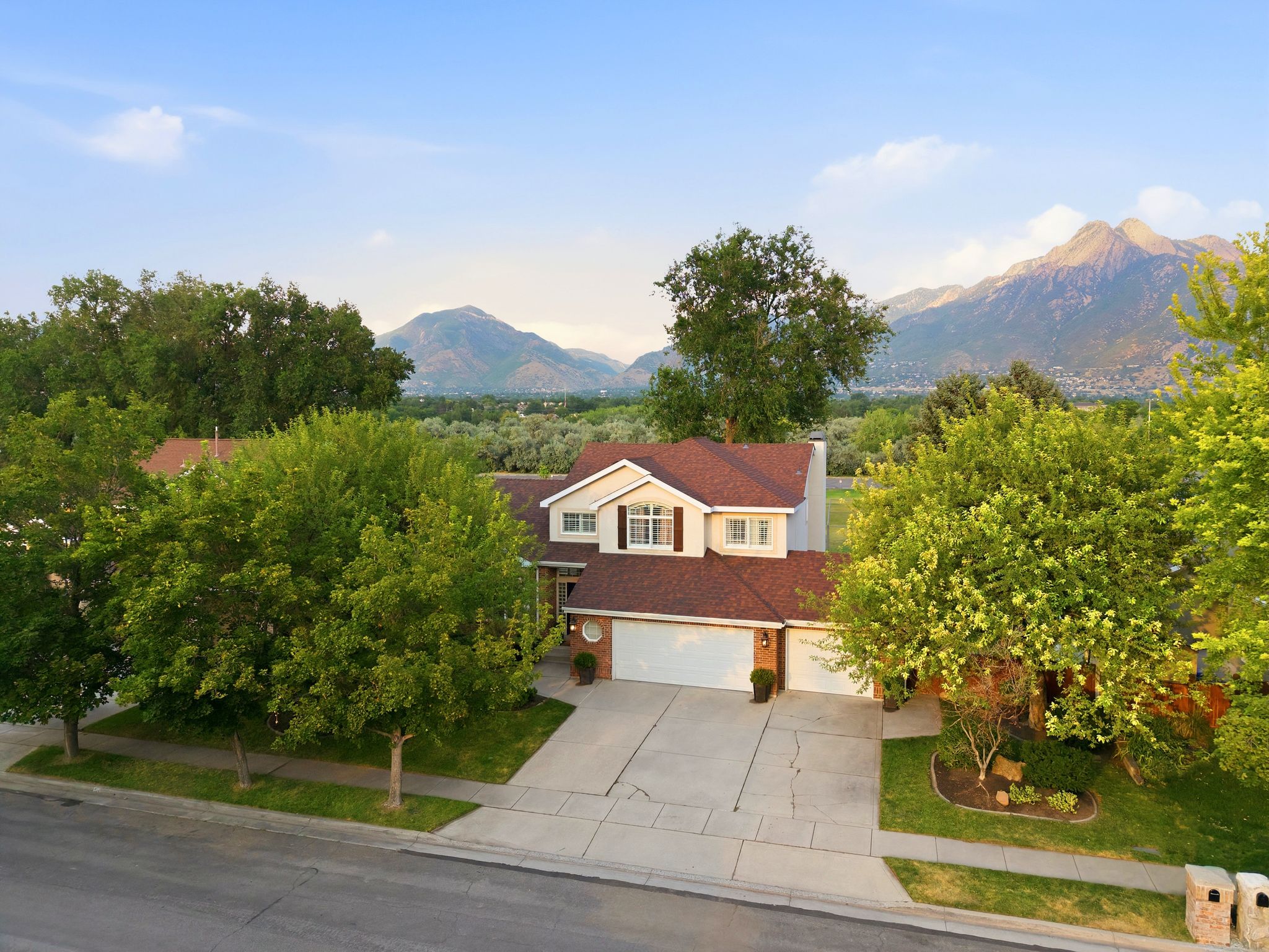 Mountain backdrop framing a classic two-story residence with a multi-car garage, mature landscaping, and an asphalt driveway