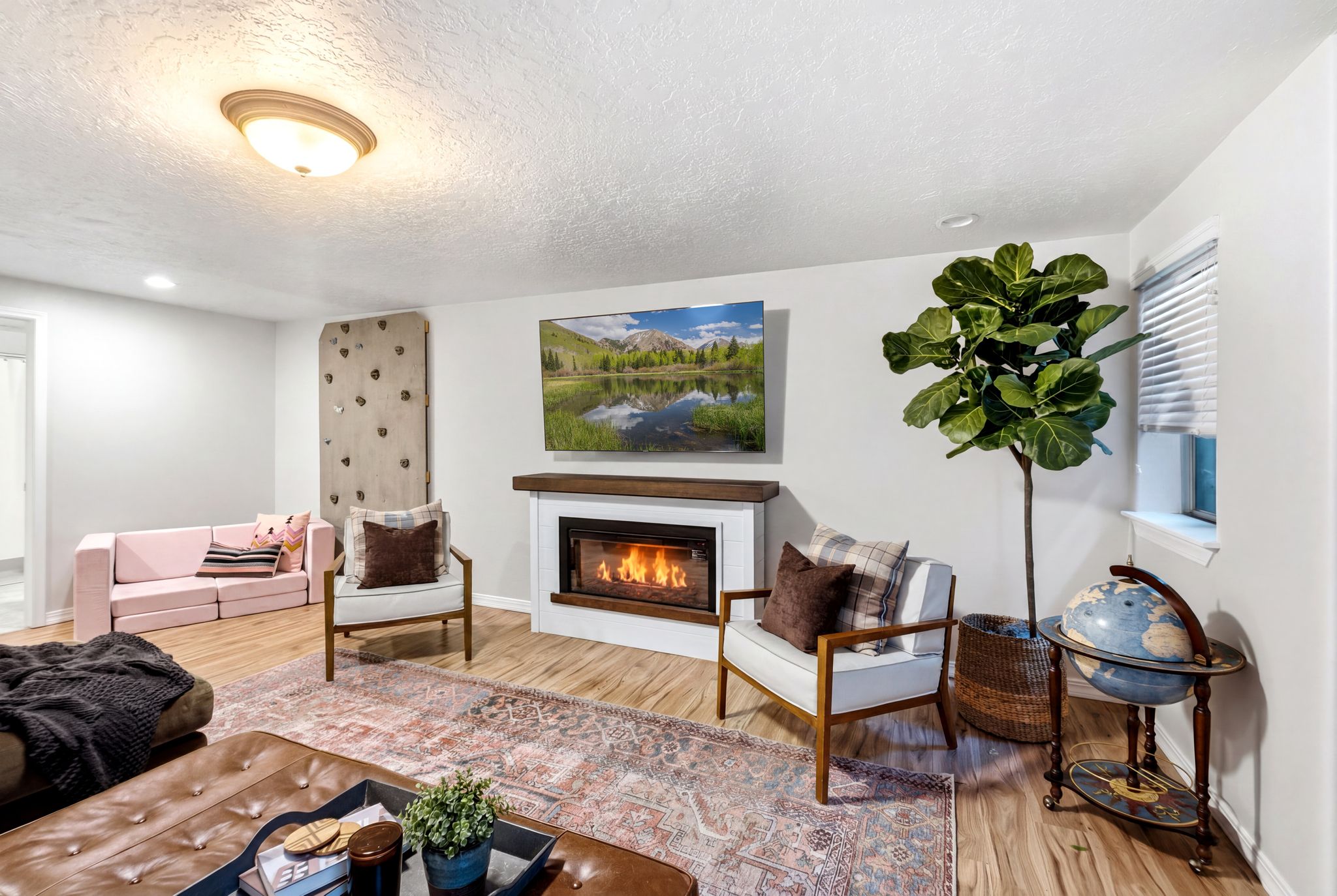 Living area featuring wood-finish flooring, a fireplace with a white surround and wood mantel, white walls, a ceiling-mounted light fixture, and a built-in climbing wall