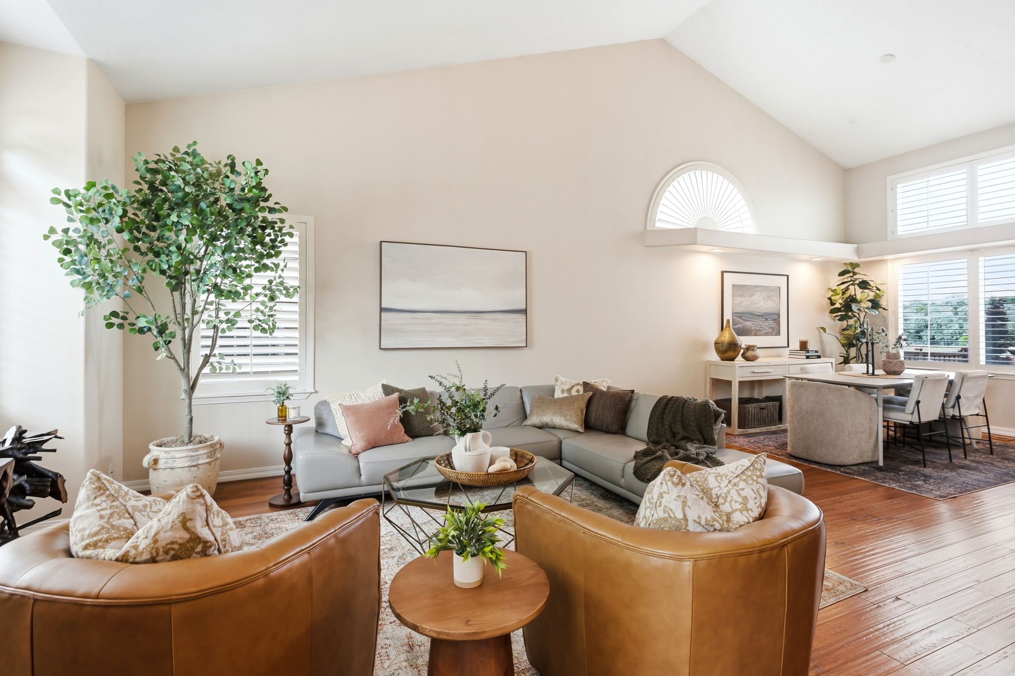 Spacious living area featuring vaulted ceilings with an arched window, rich wood-finish flooring, and multiple windows with plantation shutters