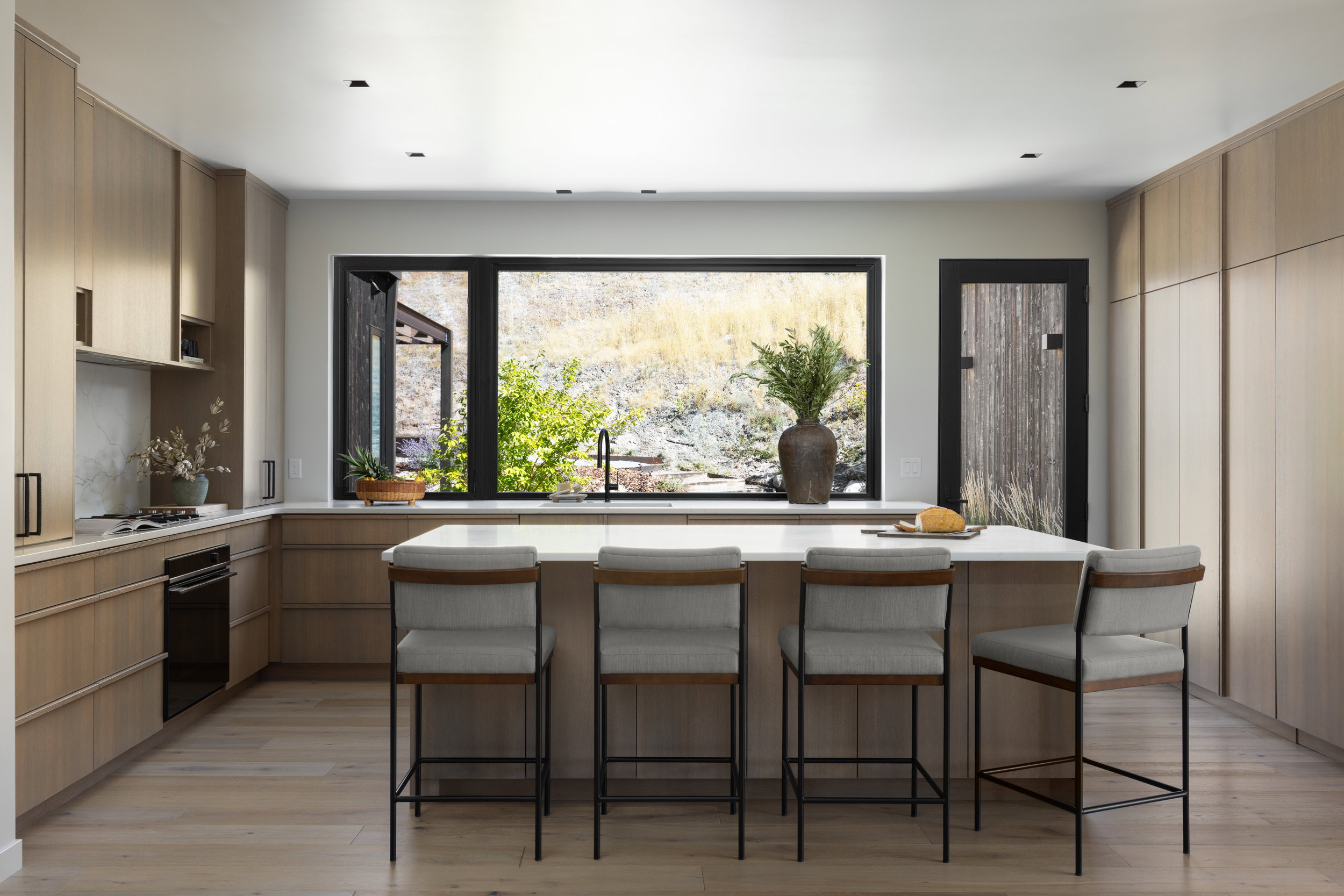 Gourmet kitchen featuring a substantial island with seating, integrated appliances, wood-finish flooring, and light wood cabinetry with ample storage