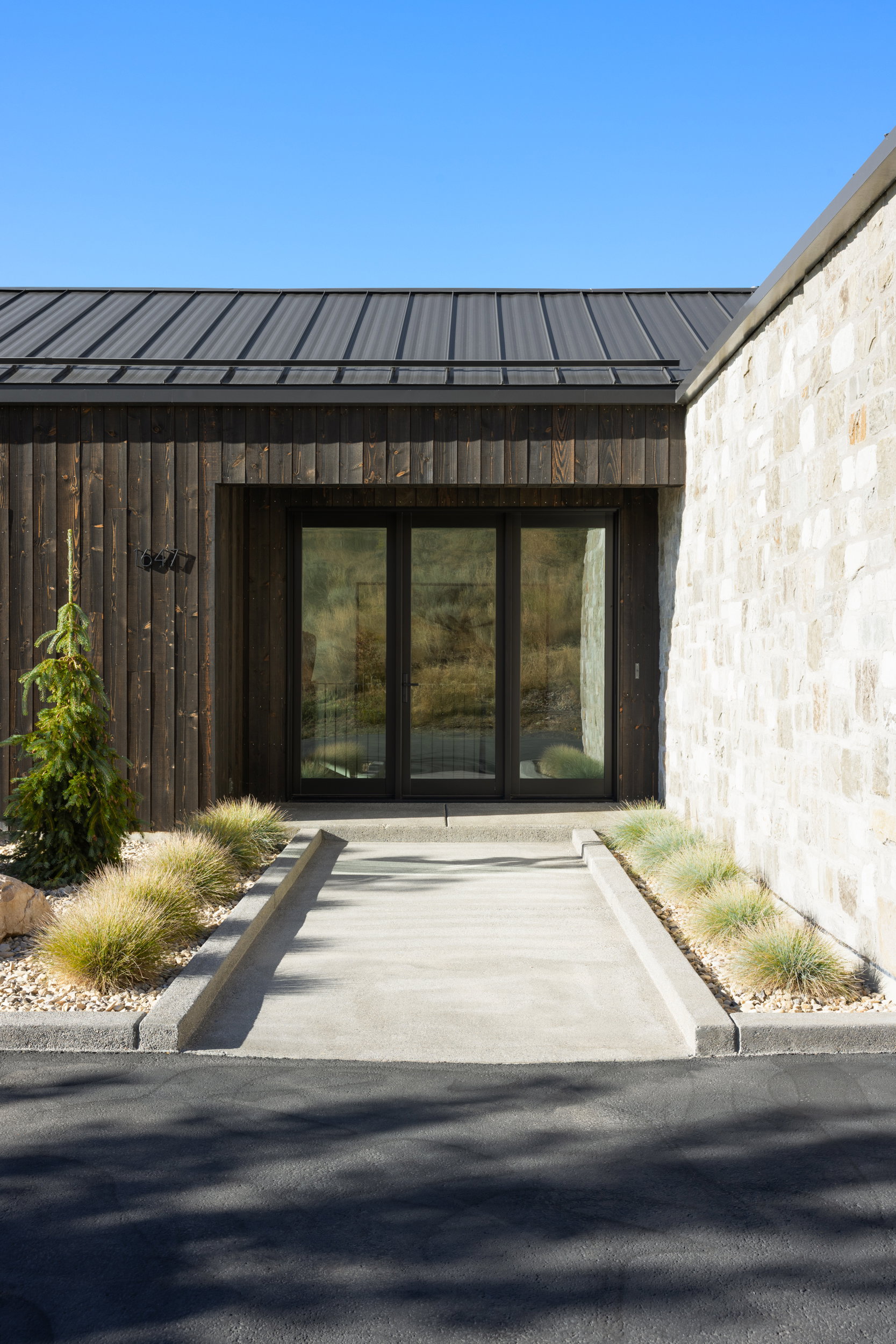 Modern exterior featuring a dark metal standing seam roof, vertical wood siding, and stone facade