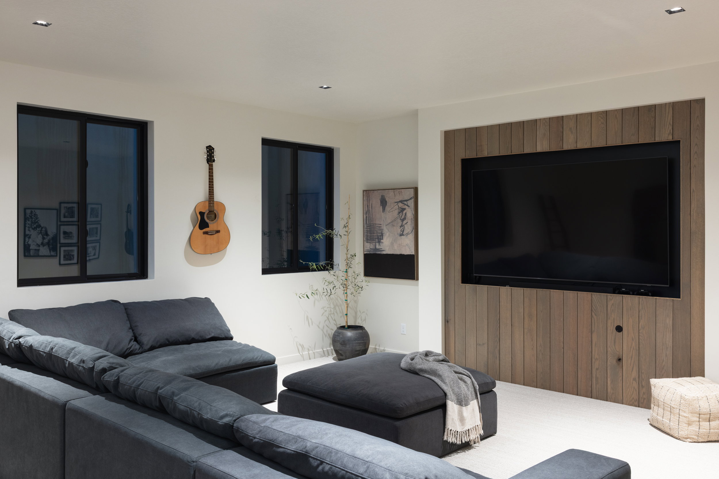Recessed television with wood-paneled feature wall, two windows with dark frames, light-colored flooring, and ceiling-mounted lighting fixtures