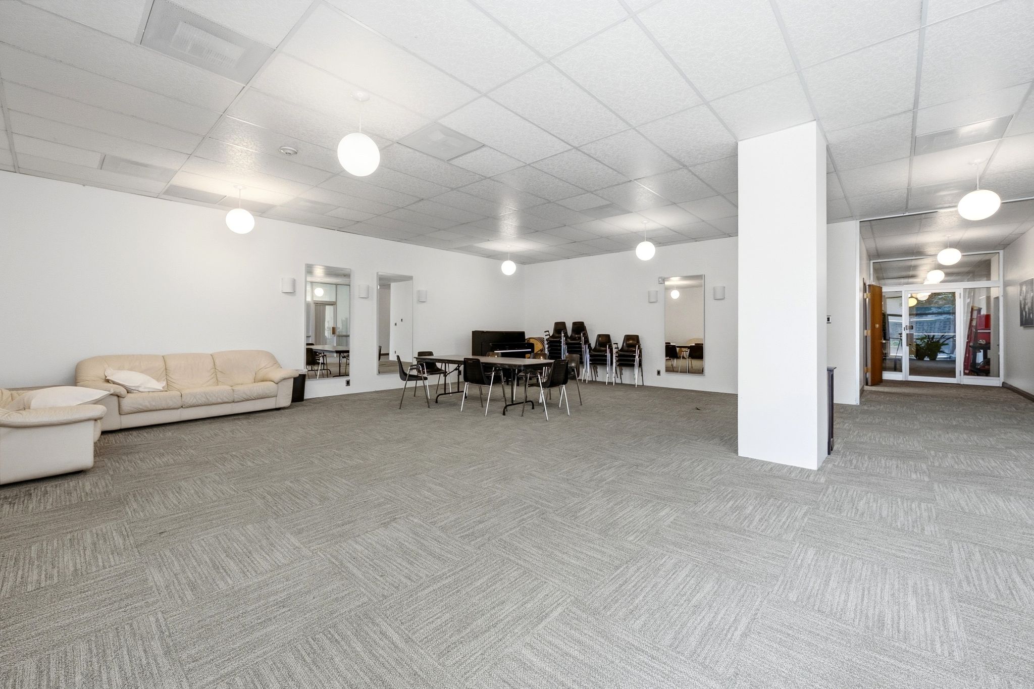Spacious common area featuring textured carpet tile flooring, a drop ceiling with recessed lighting, and multiple pendant light fixtures