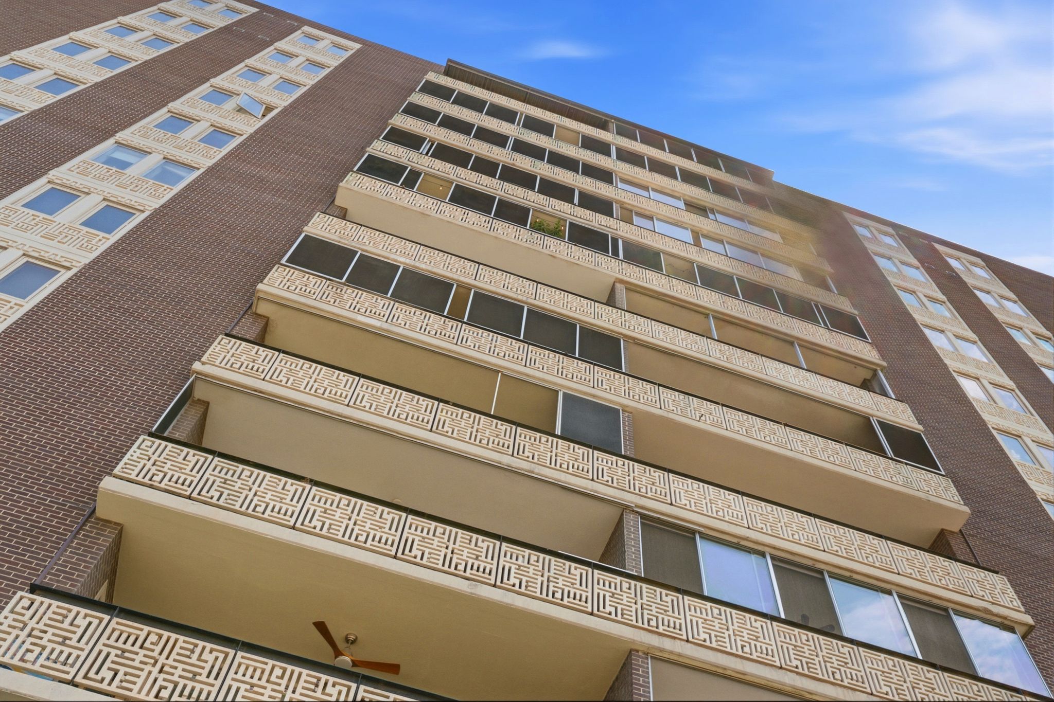 Multi-story building exterior featuring brown brick and beige architectural panels with decorative geometric patterns