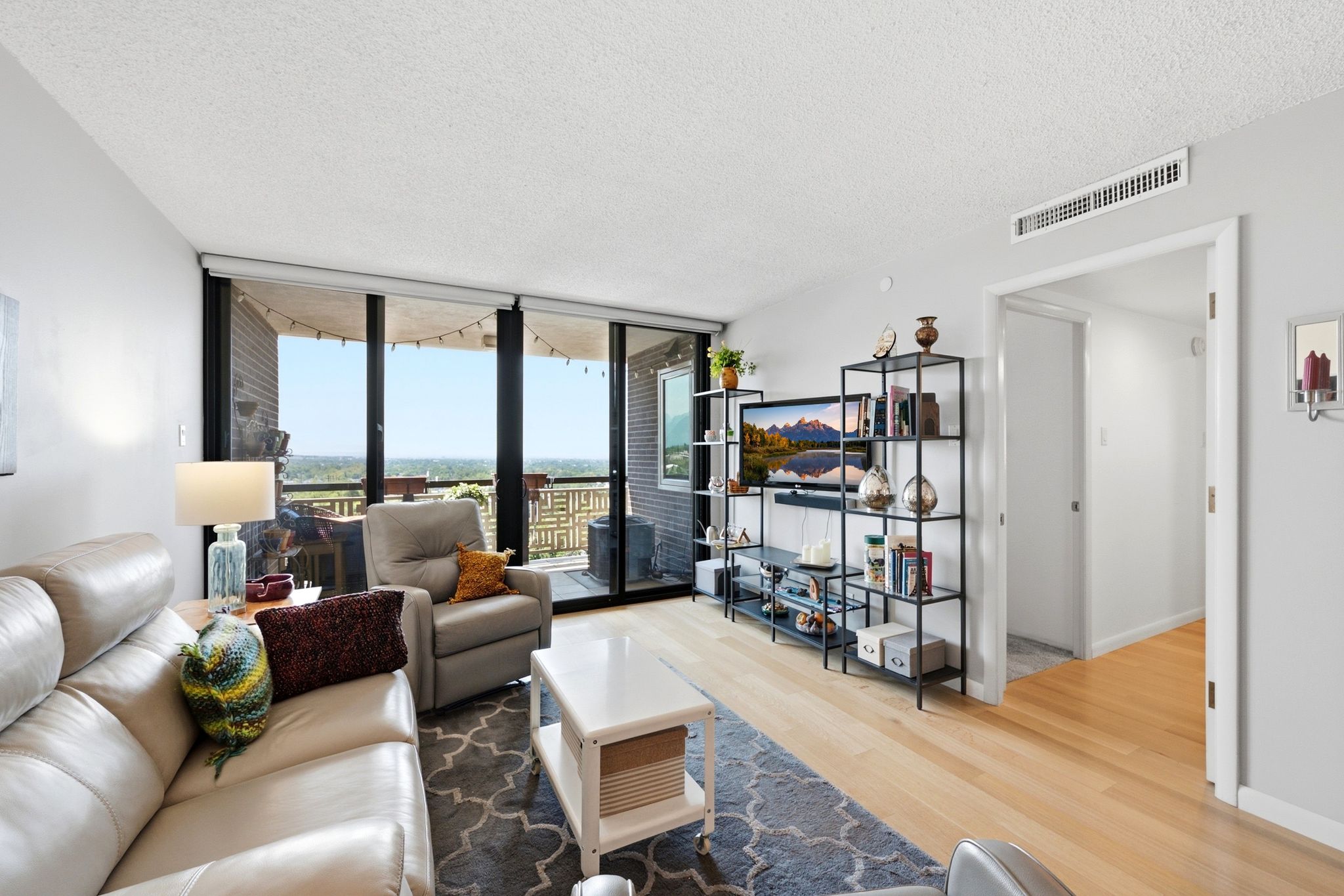 Living room featuring floor-to-ceiling windows, light wood-finish flooring, white walls, and a private balcony