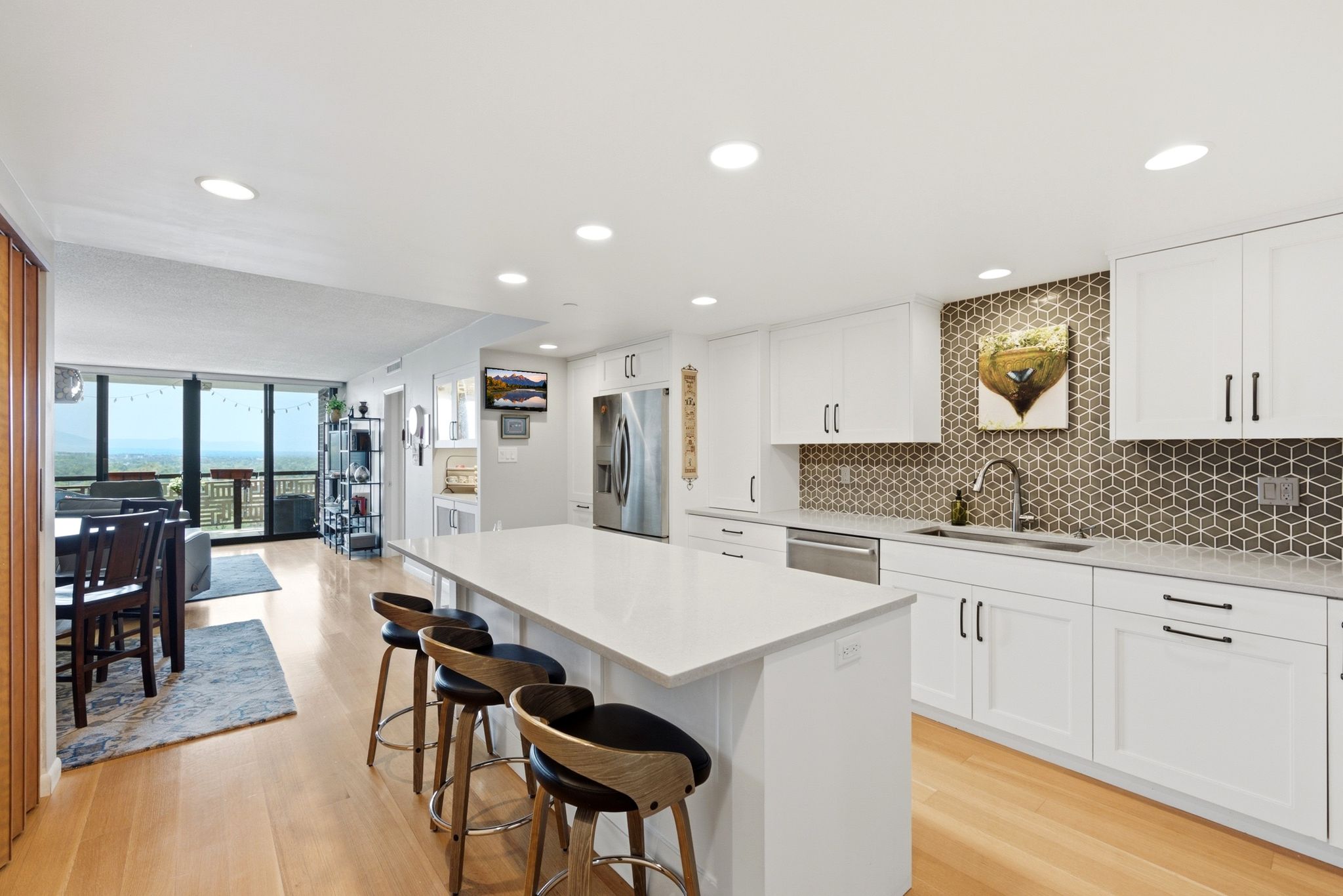 Modern kitchen featuring white cabinetry with dark hardware, a spacious island with a light-toned countertop, and a geometric pattern tile backsplash