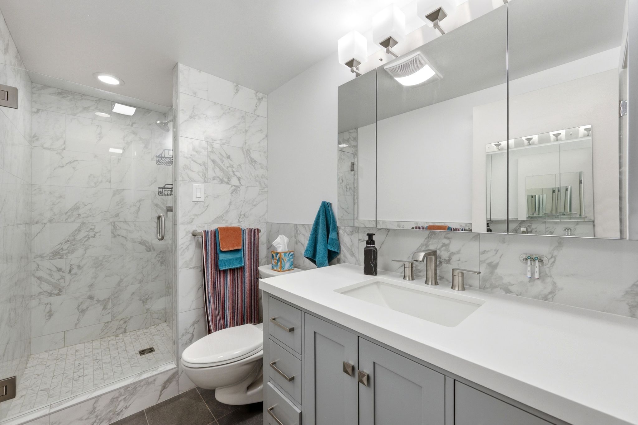 Modern bathroom featuring a glass-enclosed shower with white marble-patterned tile, a matching marble-patterned backsplash, a white rectangular undermount sink, a wide vanity with gray shaker-style cabinetry, and brushed nickel fixtures