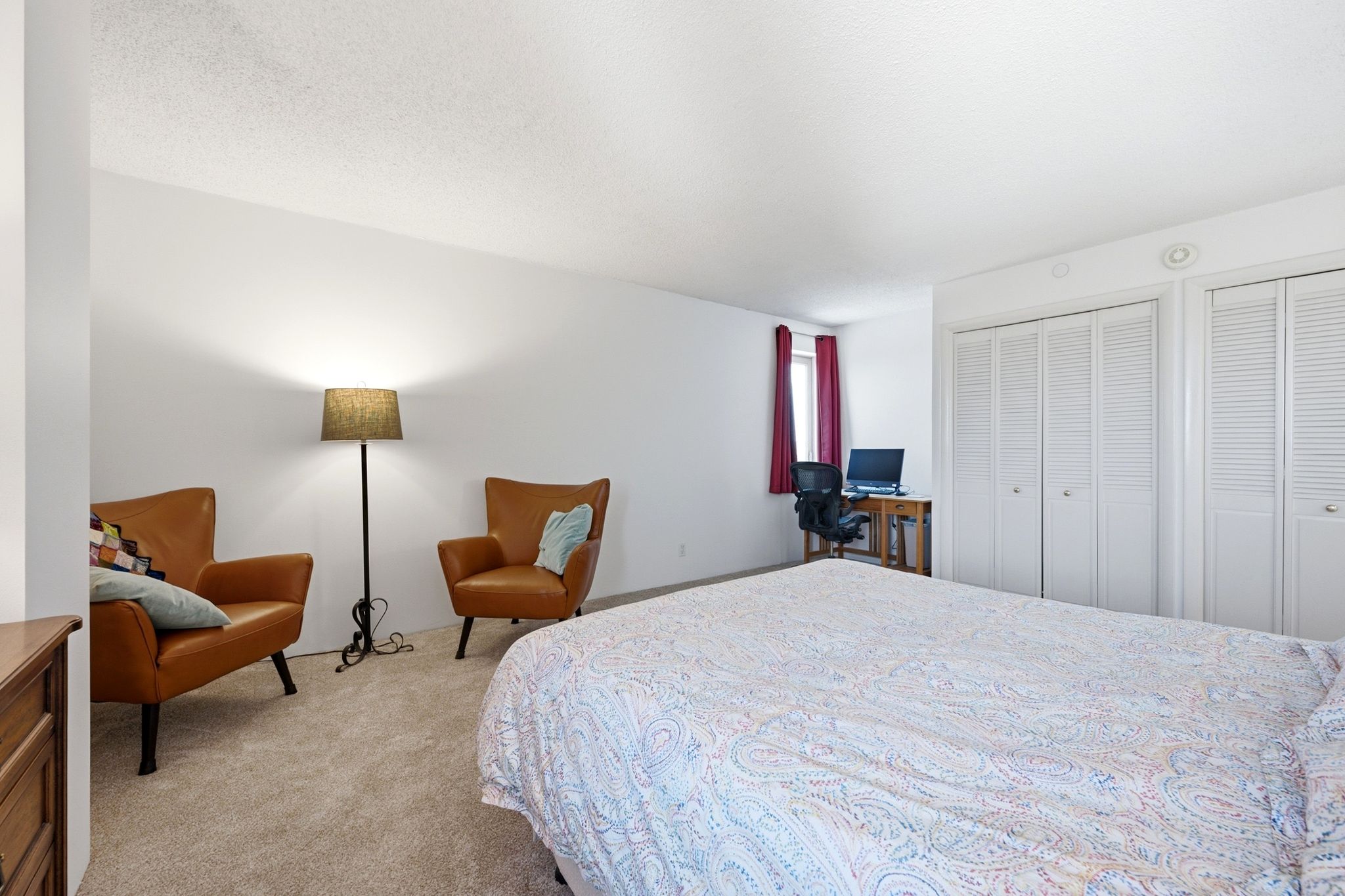 Spacious room featuring neutral carpeting, a window with red drapes, and two sets of bi-fold louvered closet doors