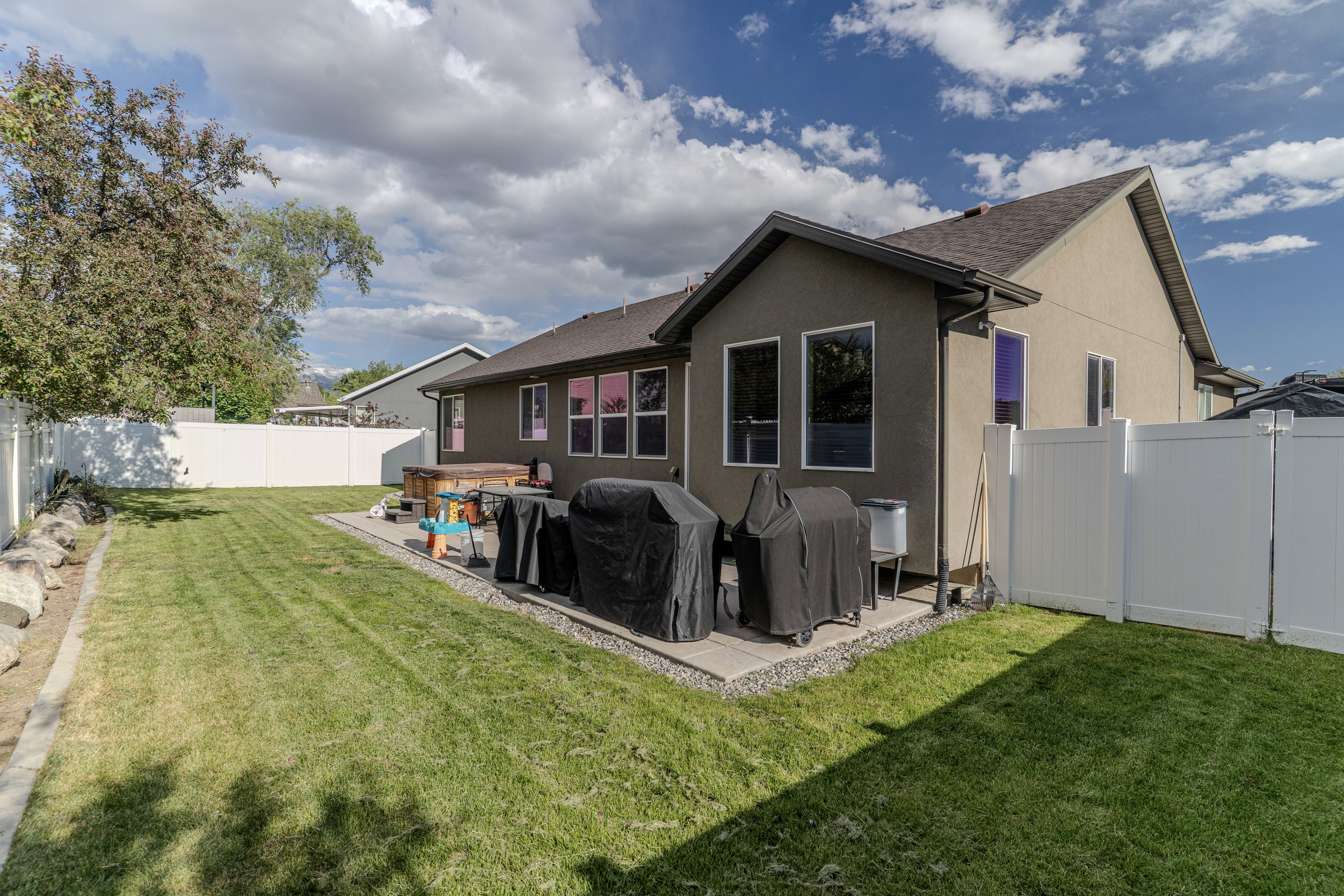 Spacious backyard featuring a large green lawn, a white privacy fence, and mature trees
