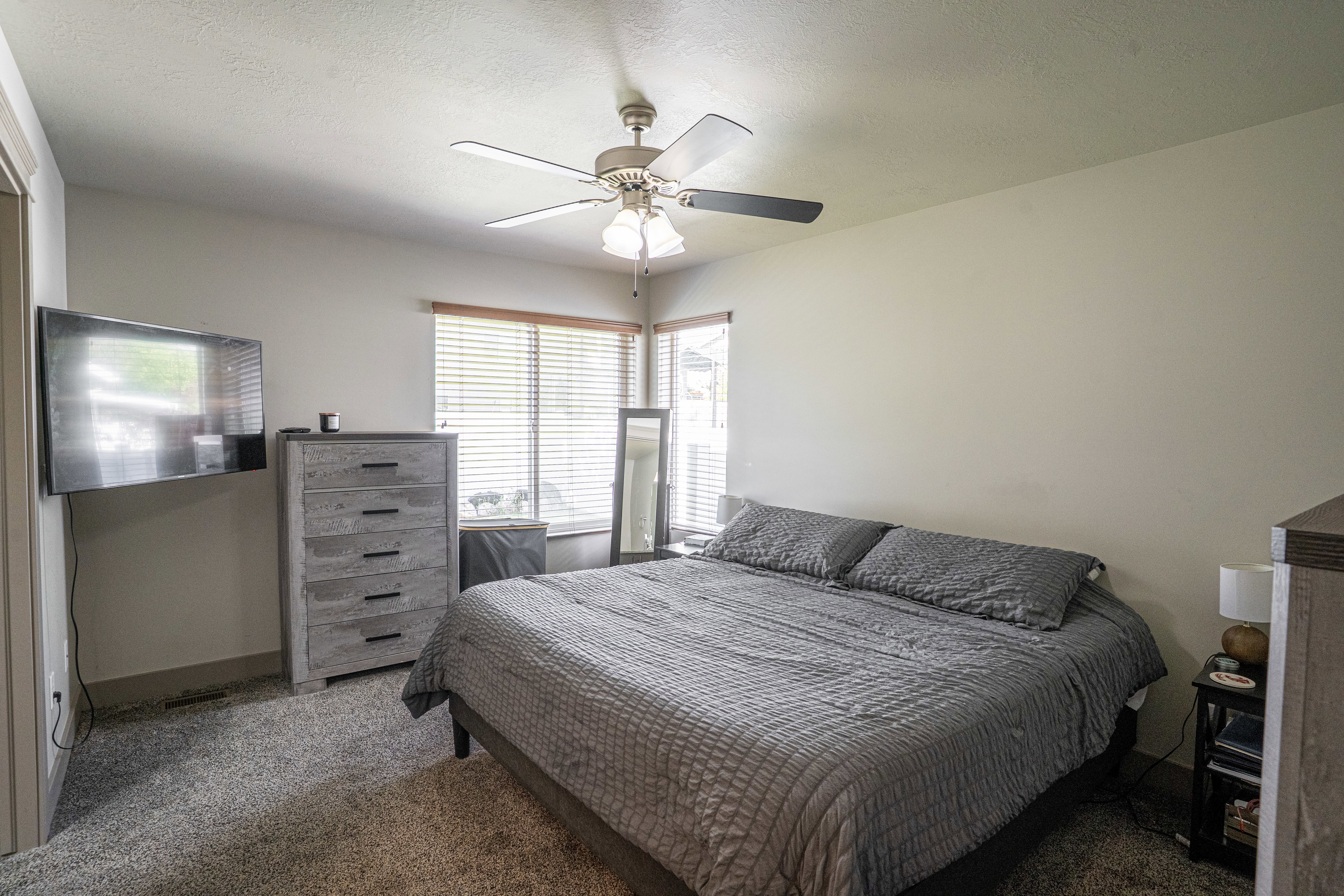 Carpeted room featuring a ceiling fan with integrated lighting, wood-finish window blinds, and light-toned wall paint