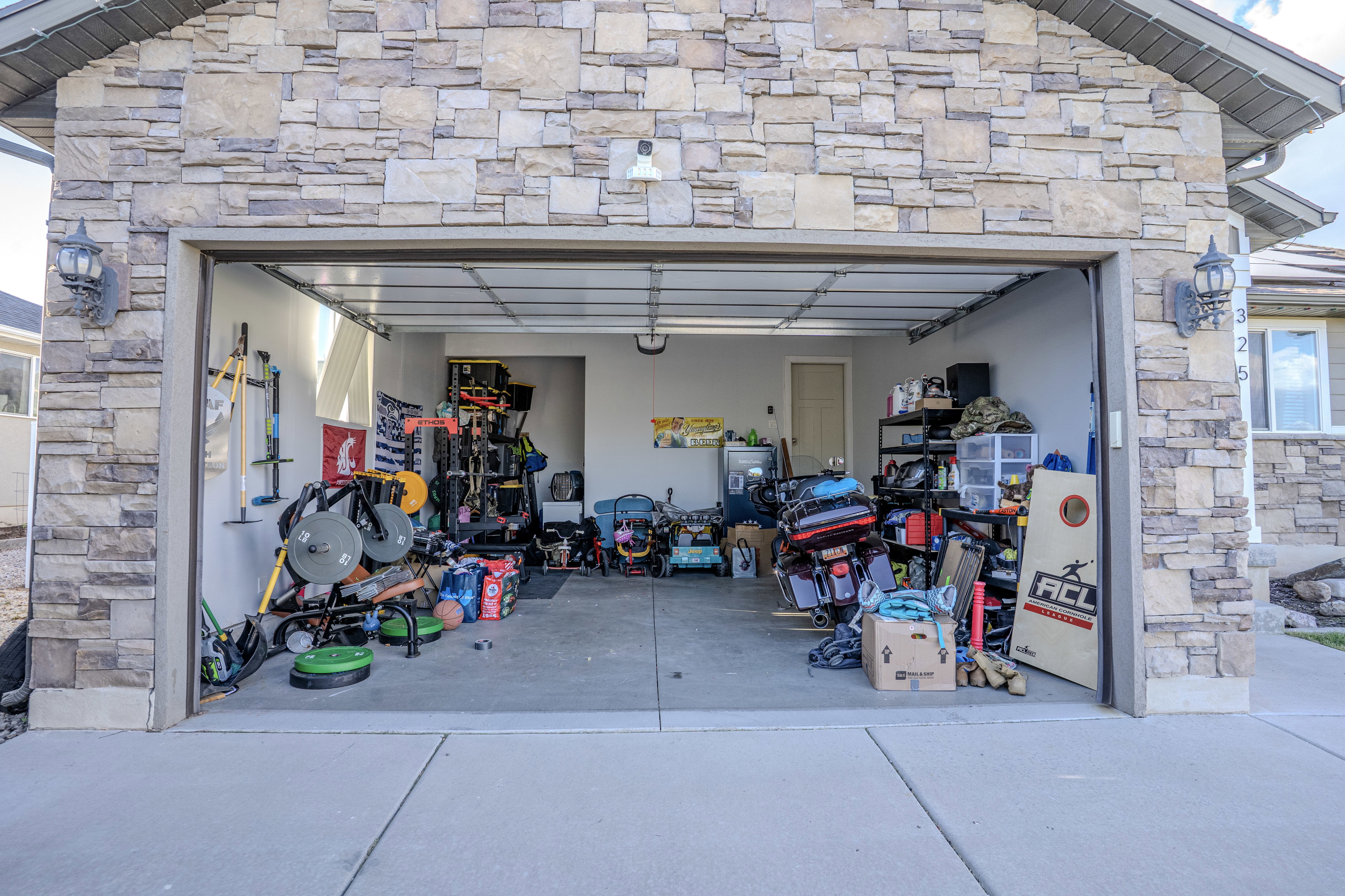 Two-car garage featuring a concrete floor, light stone exterior, two exterior sconces, and a side window