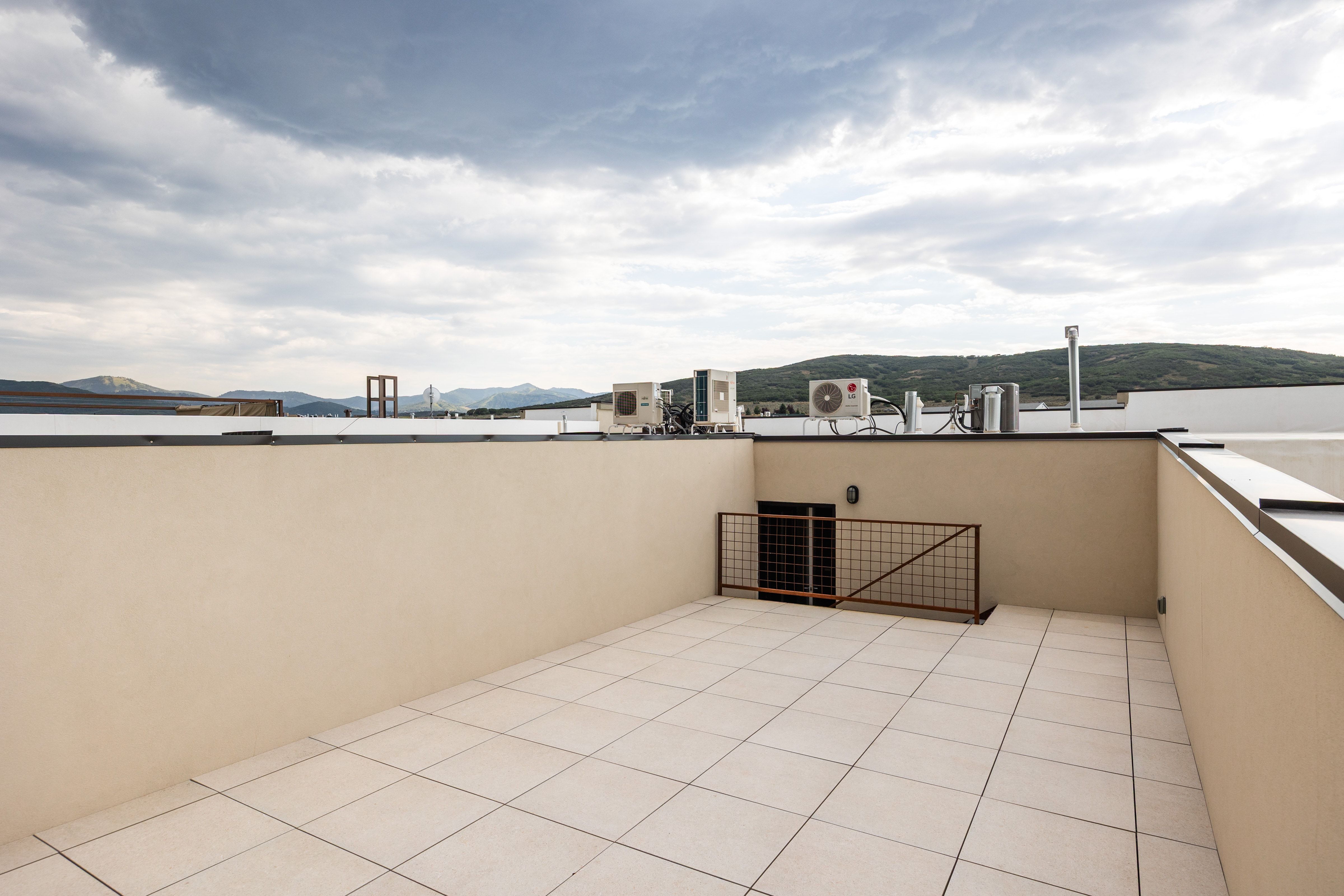 Rooftop terrace with light-colored tile flooring, parapet walls, and a distant mountain backdrop