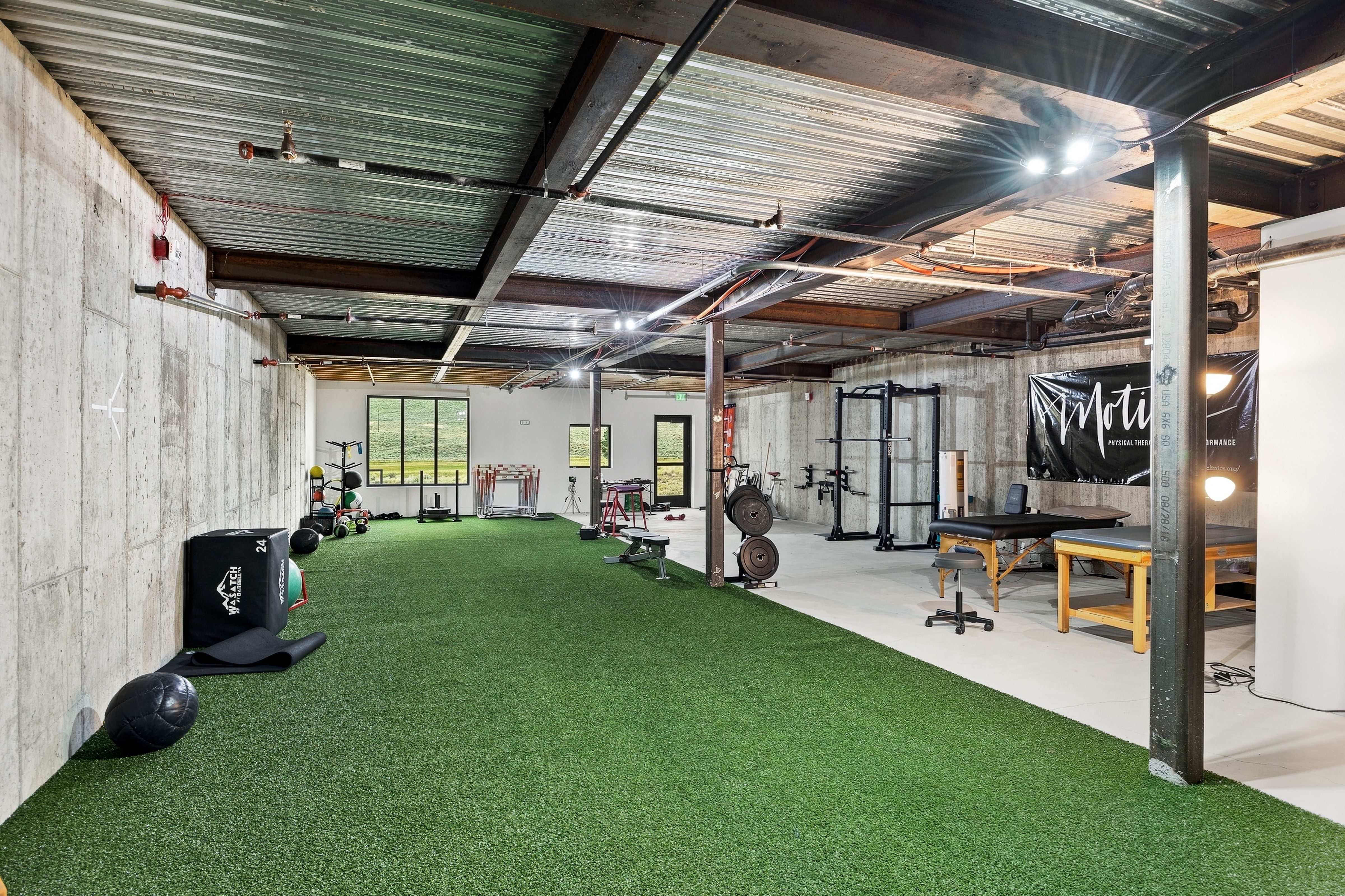 Spacious multi-purpose room featuring a concrete foundation, exposed structural beams, and a combination of artificial turf and concrete flooring