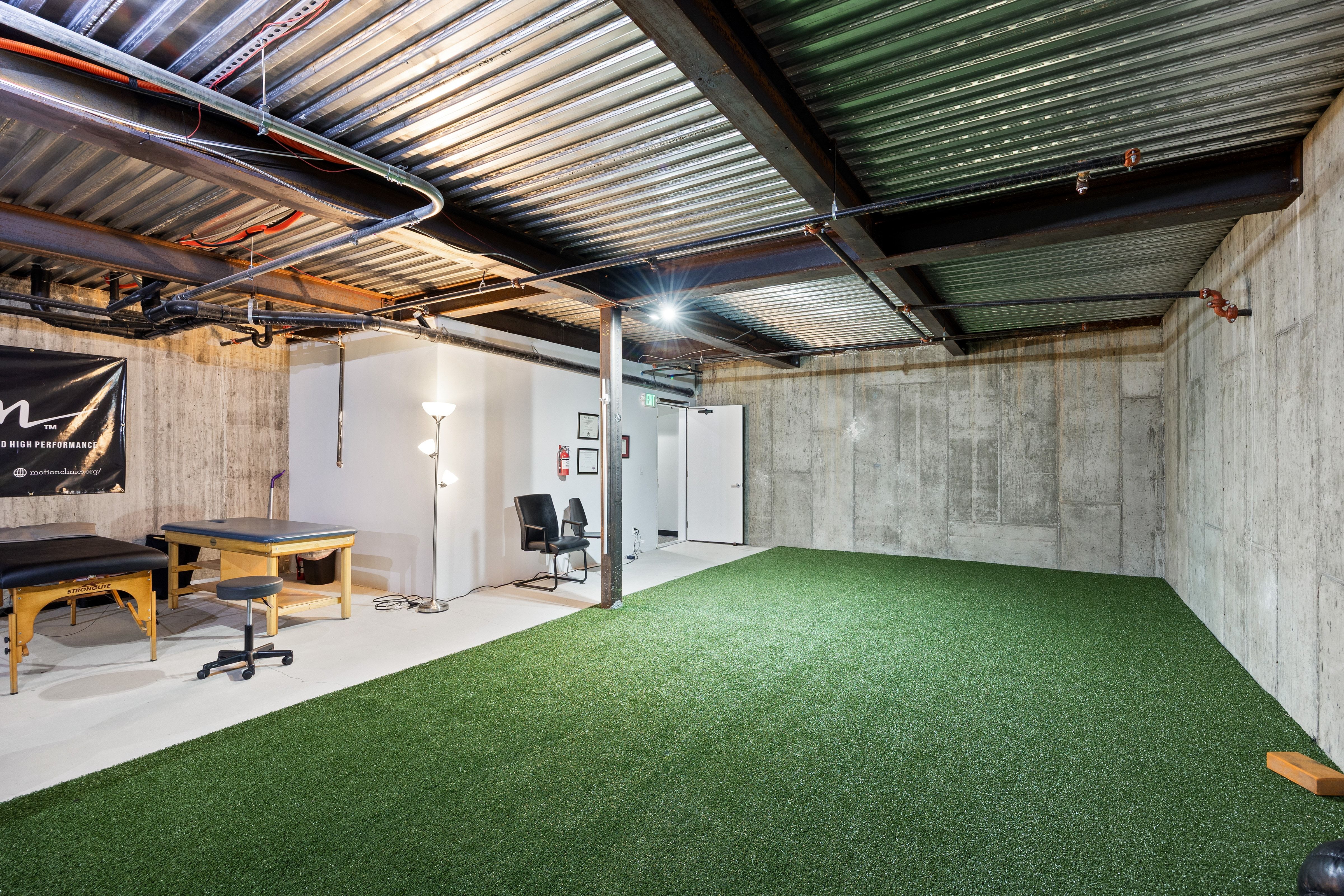 Expansive basement area featuring an artificial turf surface and exposed corrugated metal ceiling