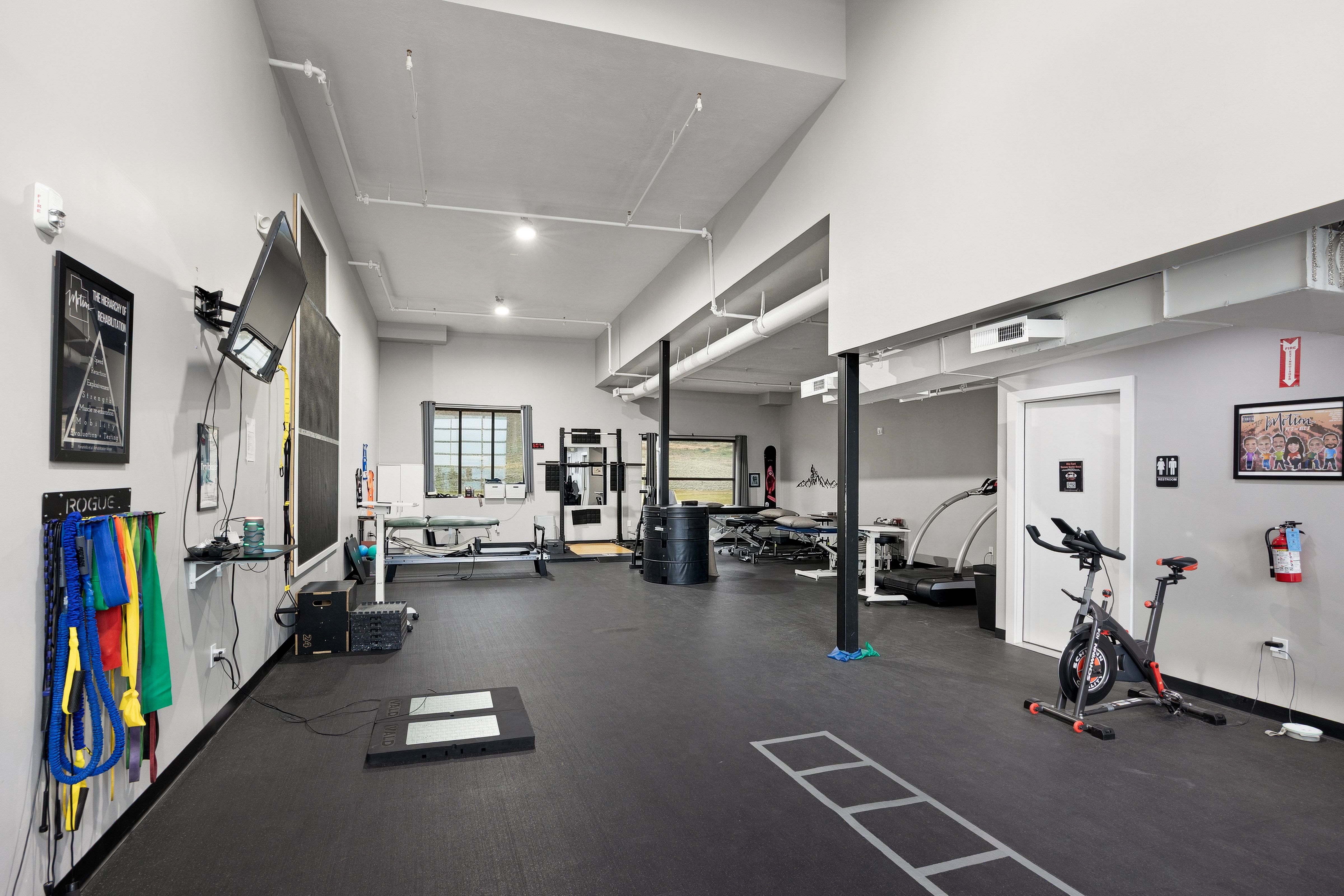 Spacious interior featuring high ceilings with exposed ductwork, resilient black flooring, and multiple windows providing natural illumination