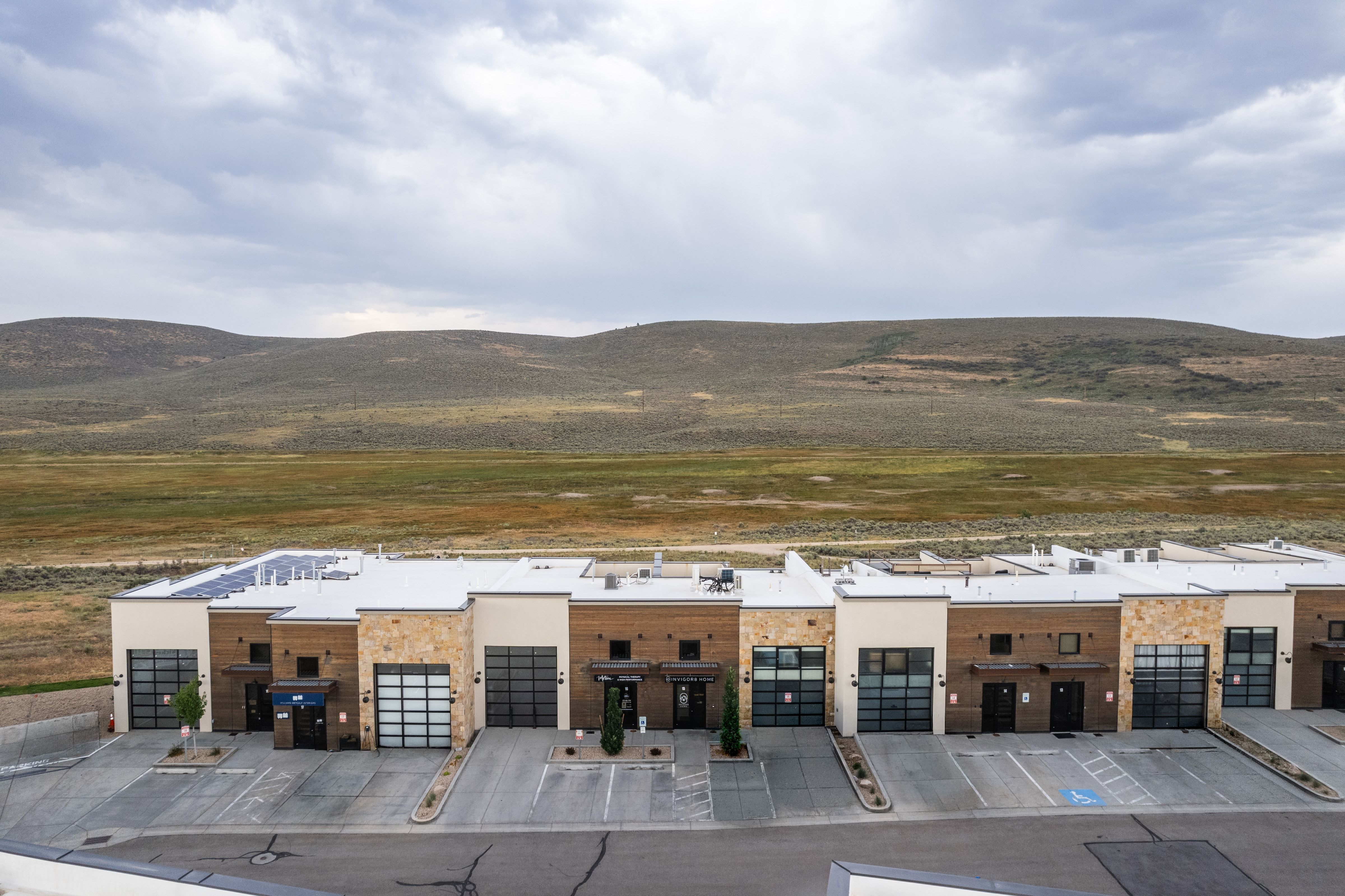 Contemporary multi-unit structure featuring a flat roof with solar panels, stone and wood-tone exterior accents, glass-paneled overhead doors, and individual entryways