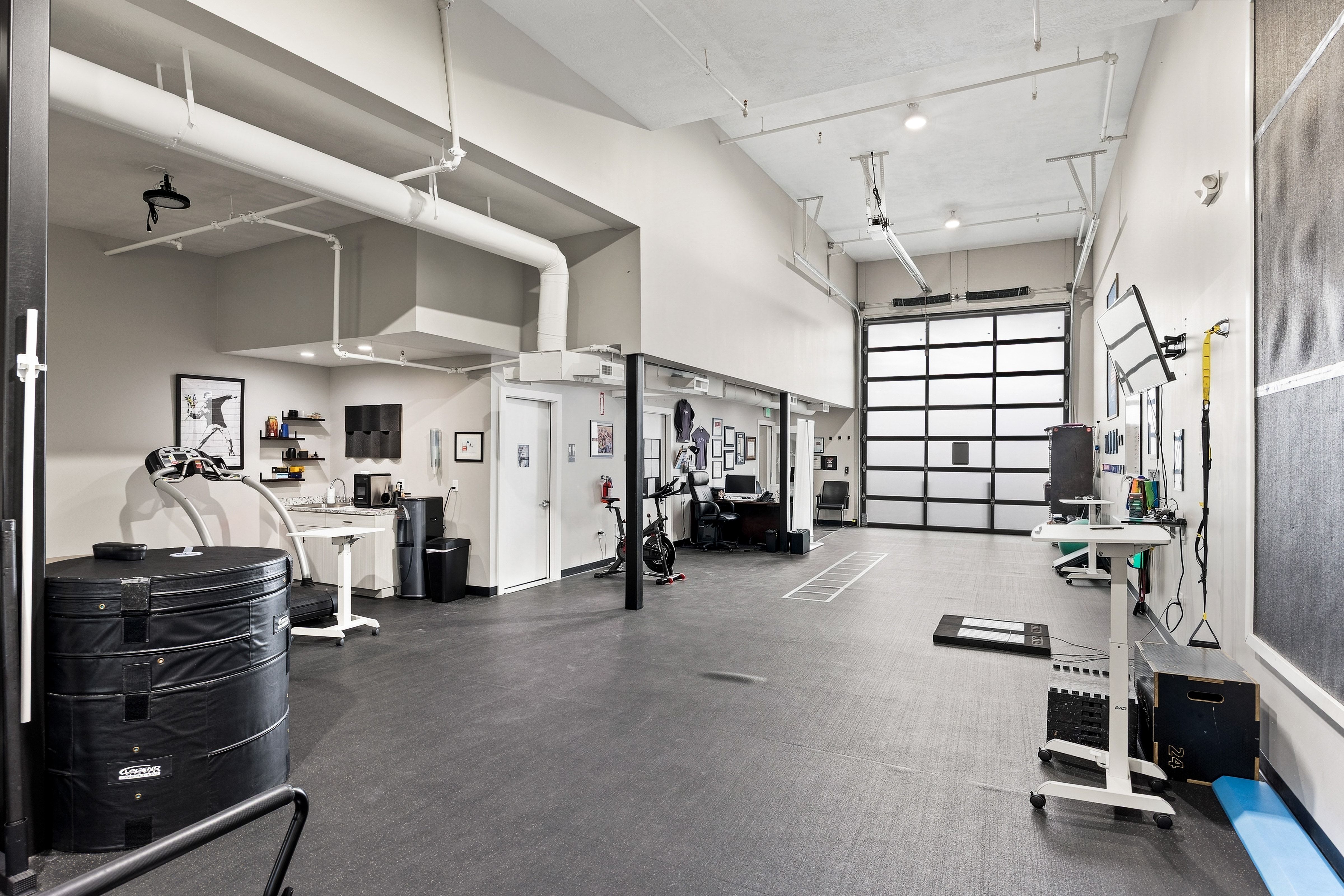 Spacious interior featuring a large overhead door, exposed industrial ductwork, high ceilings, and durable rubberized flooring