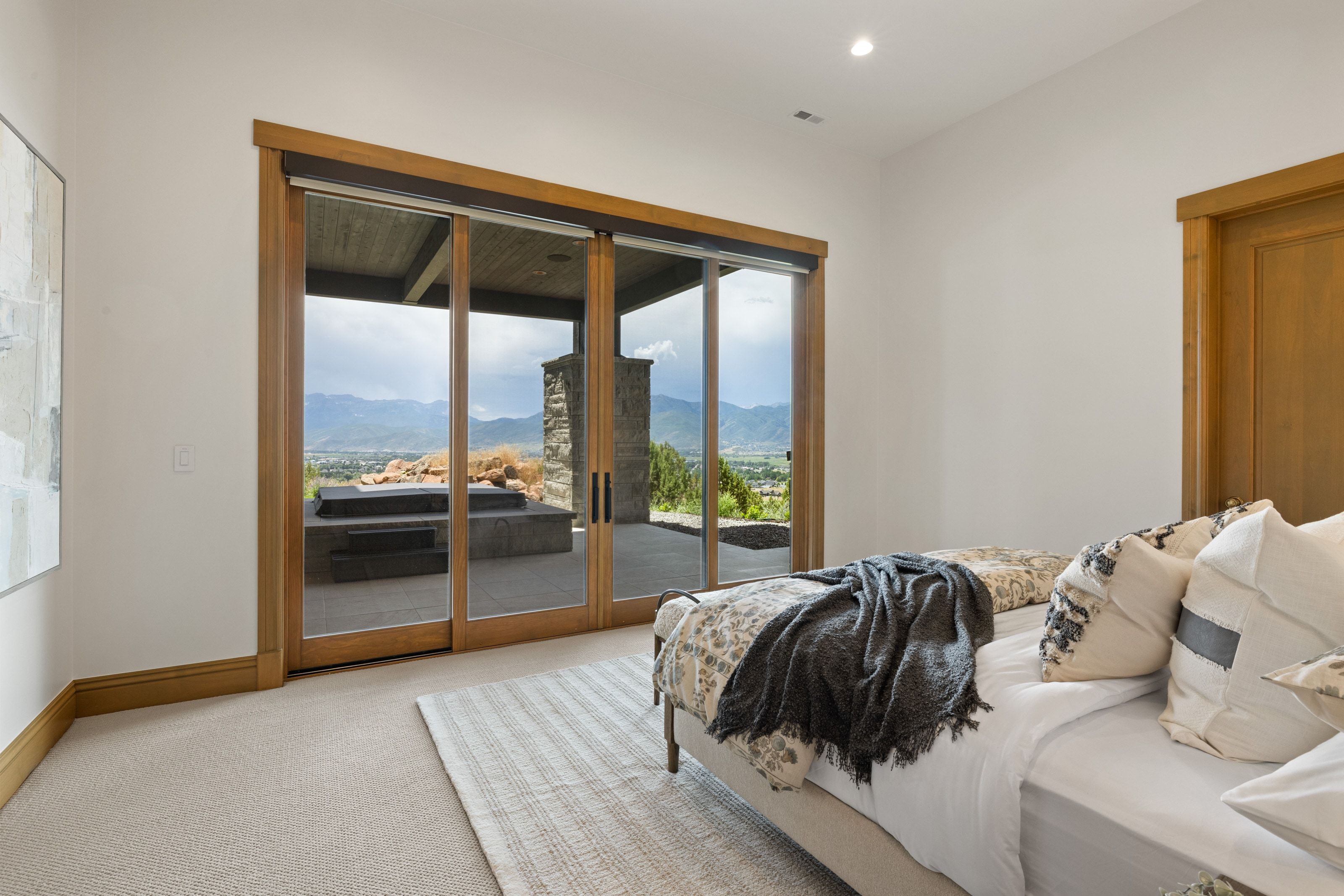 Expansive sliding glass doors with natural wood frames open to an outdoor patio with mountain scenery