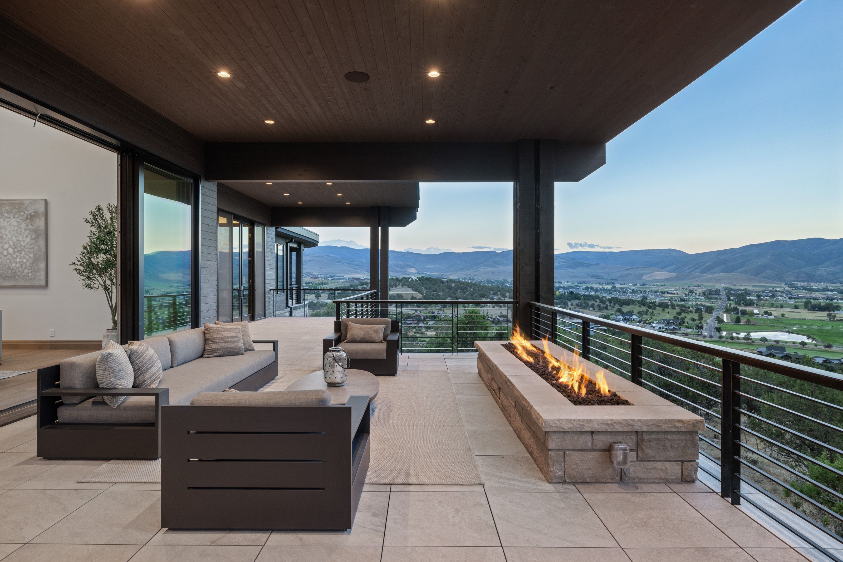 Expansive outdoor terrace featuring a built-in stone fire pit, cable railing system, and a wood-paneled ceiling with recessed lighting