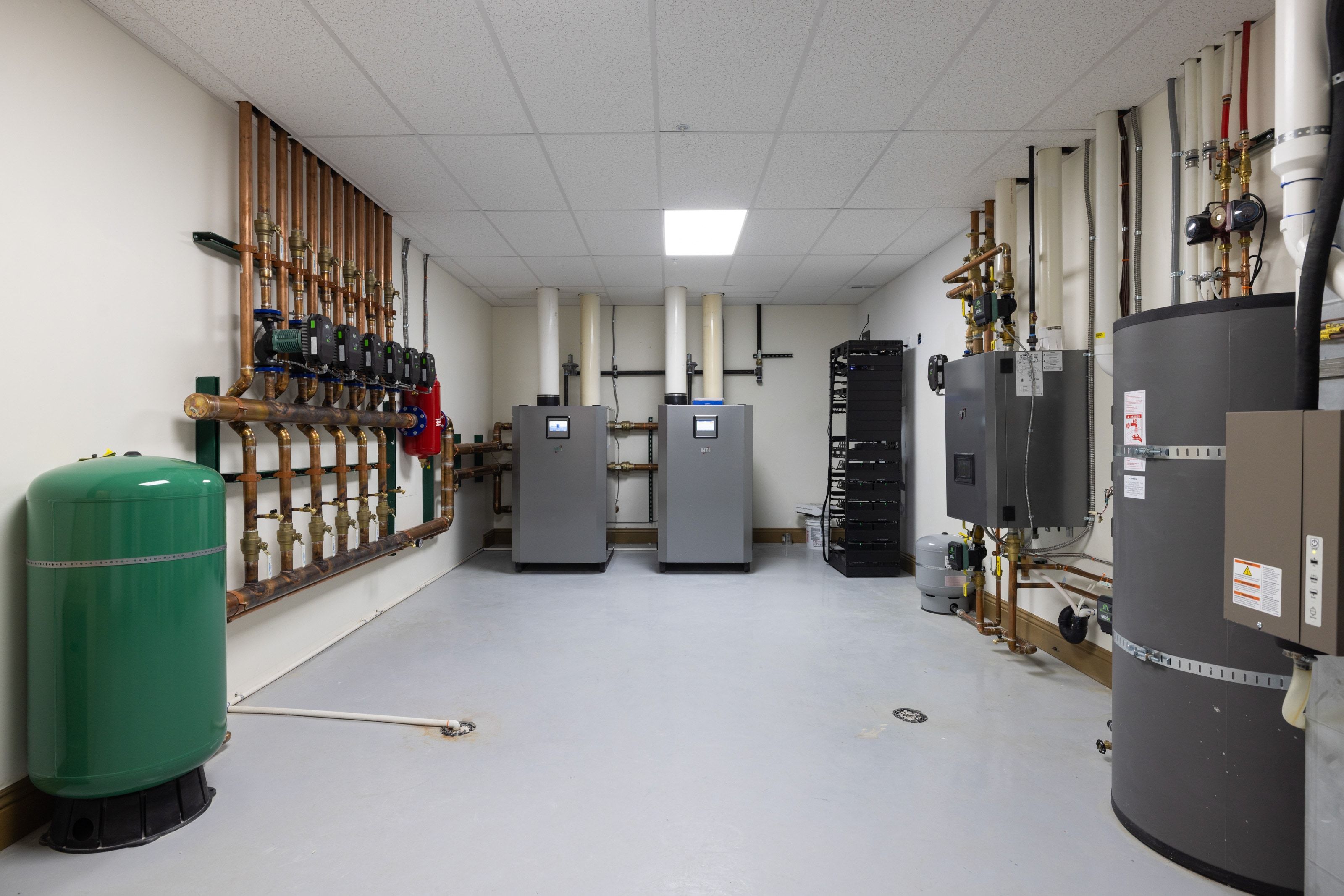 Dedicated utility room featuring comprehensive mechanical systems, including a pressurized expansion tank, multiple copper pipe manifolds, two water heaters, and a rack-mounted system