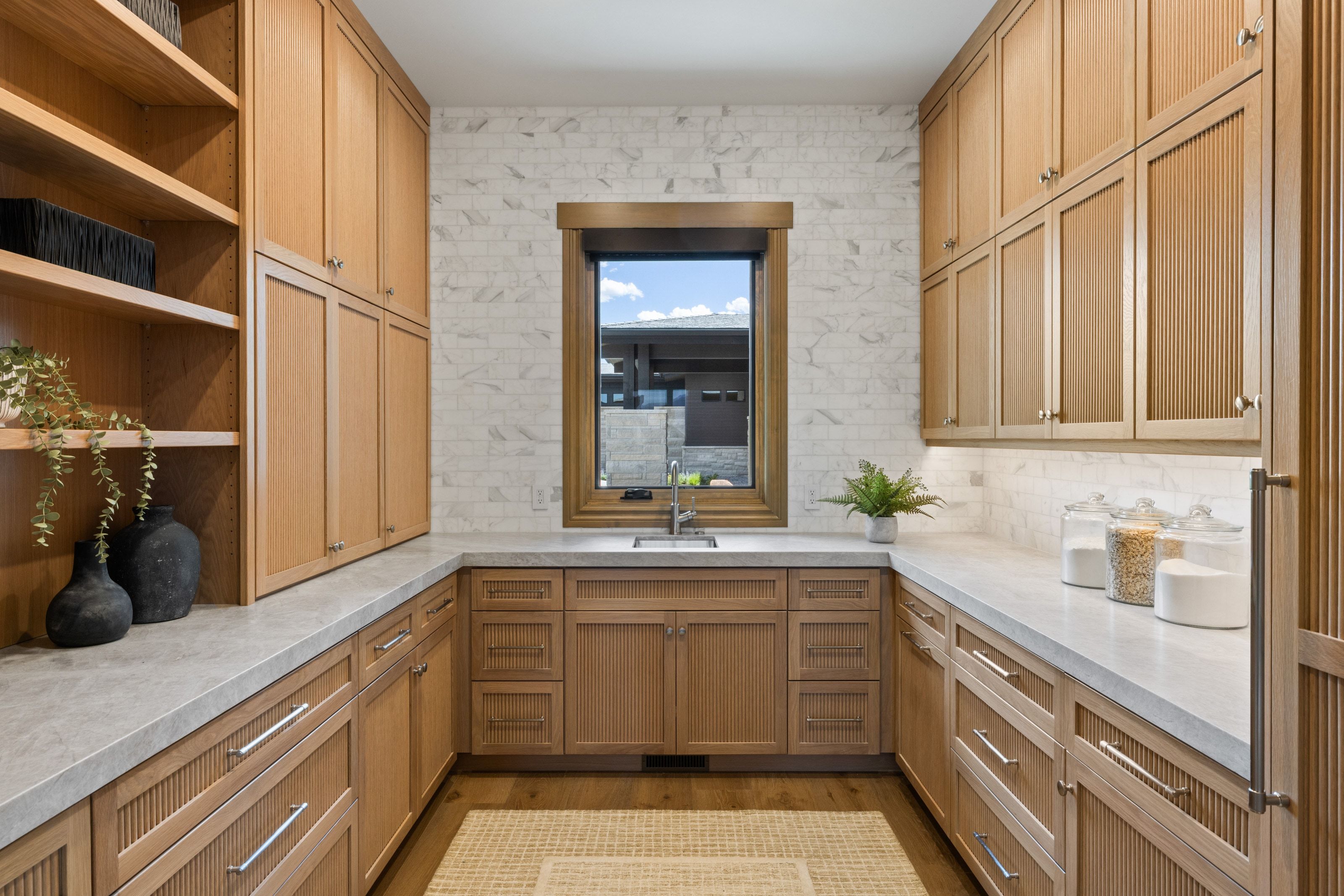 Kitchen pantry featuring extensive wood-finish cabinetry, open shelving, and light stone-look countertops