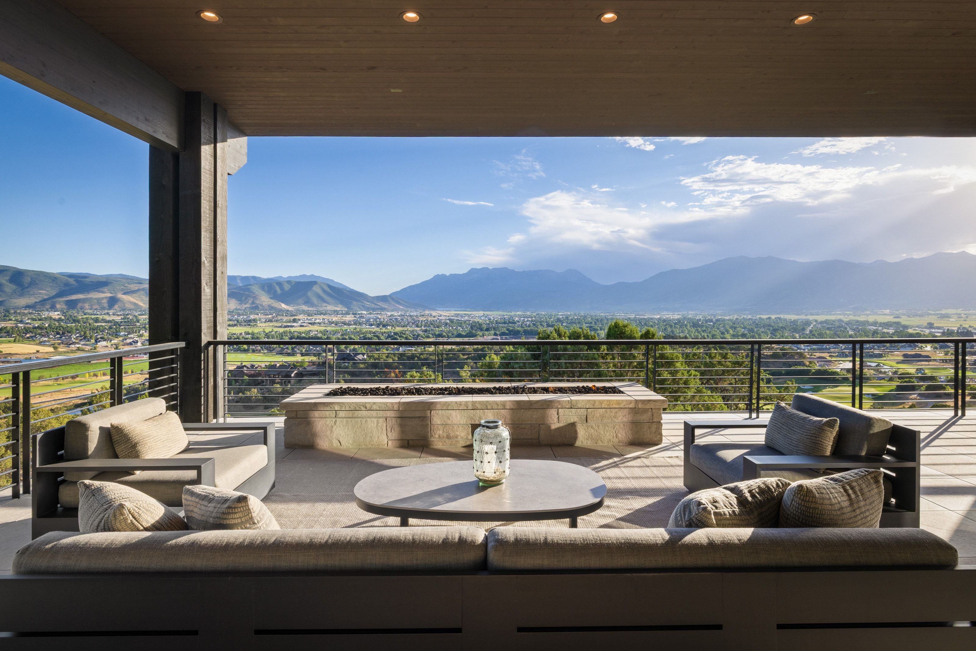 Expansive outdoor living space featuring a stone fire pit, wood-finish ceiling with recessed lighting, and cable railing