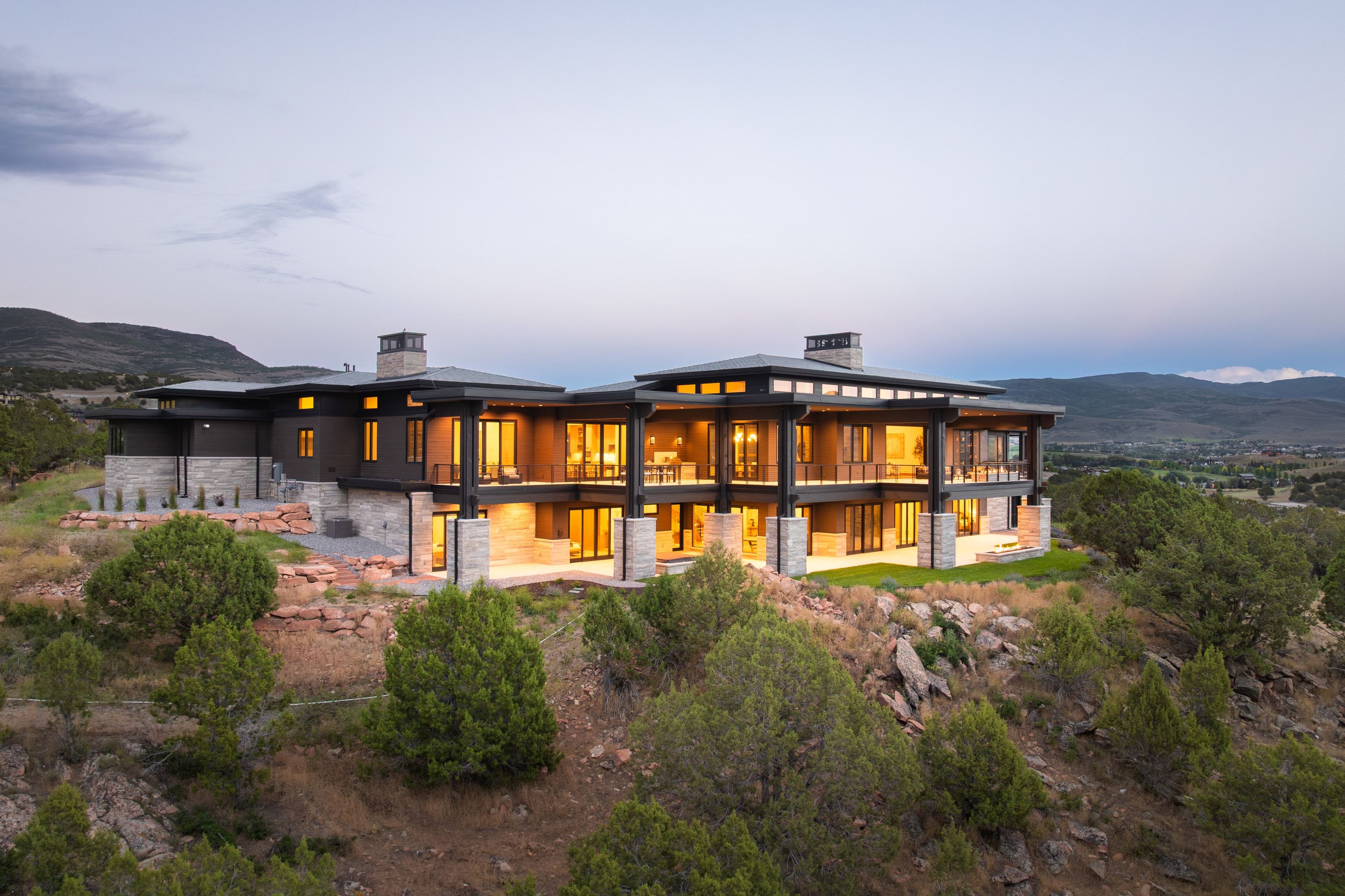 Contemporary multi-level residence featuring expansive window walls, stone accents, and multiple outdoor patio areas