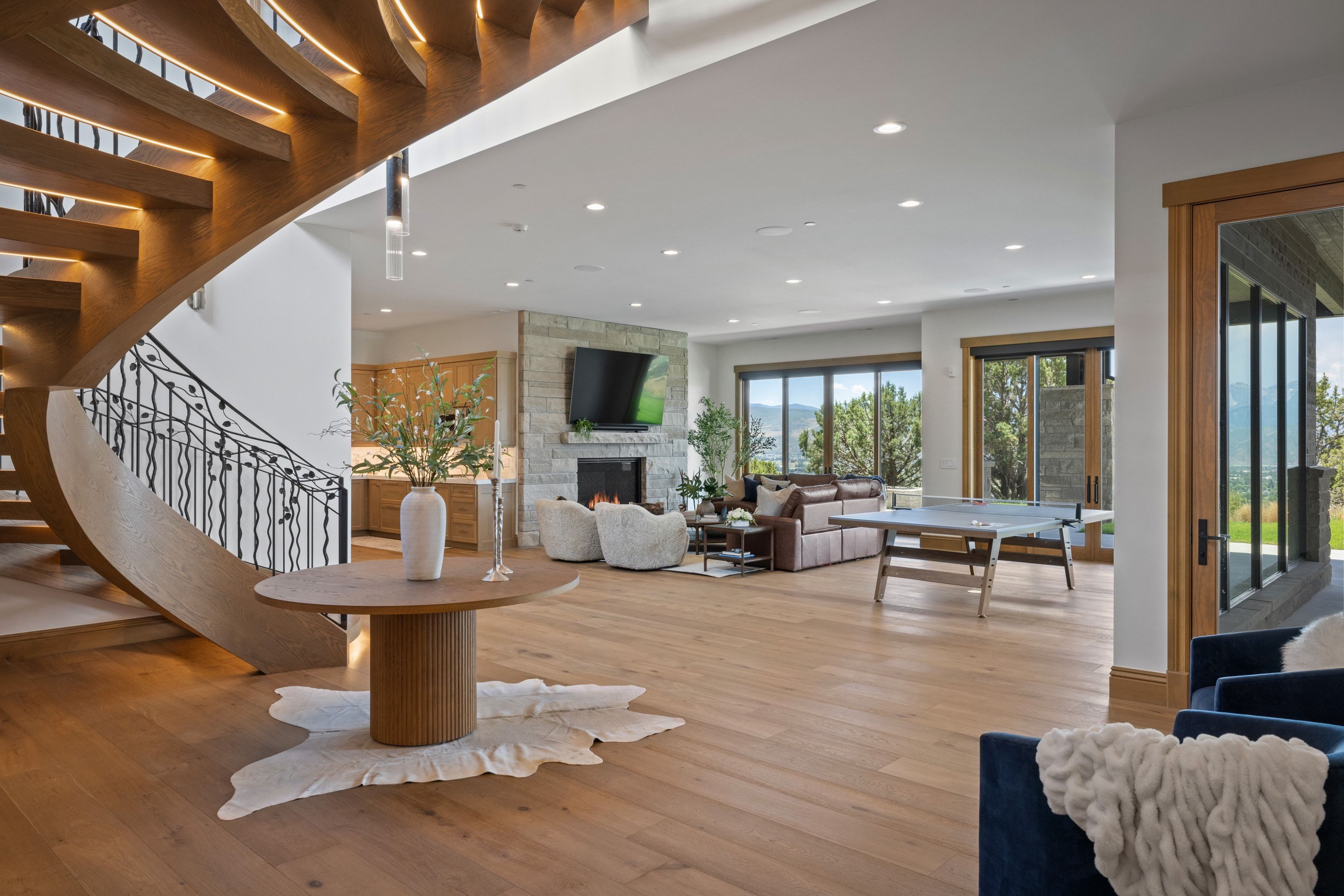 Curved wood staircase with wrought iron railing, light wood-finish flooring, recessed lighting, stone fireplace, and large sliding glass doors