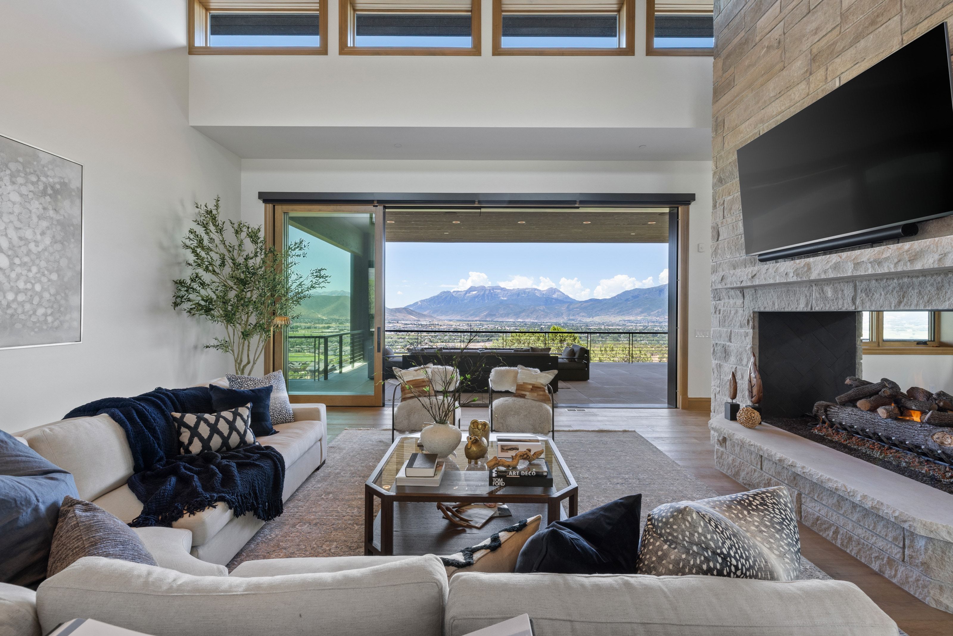 Spacious living area featuring a floor-to-ceiling stone fireplace, high ceilings, wood-finish flooring, and a large sliding glass door opening to a substantial outdoor patio