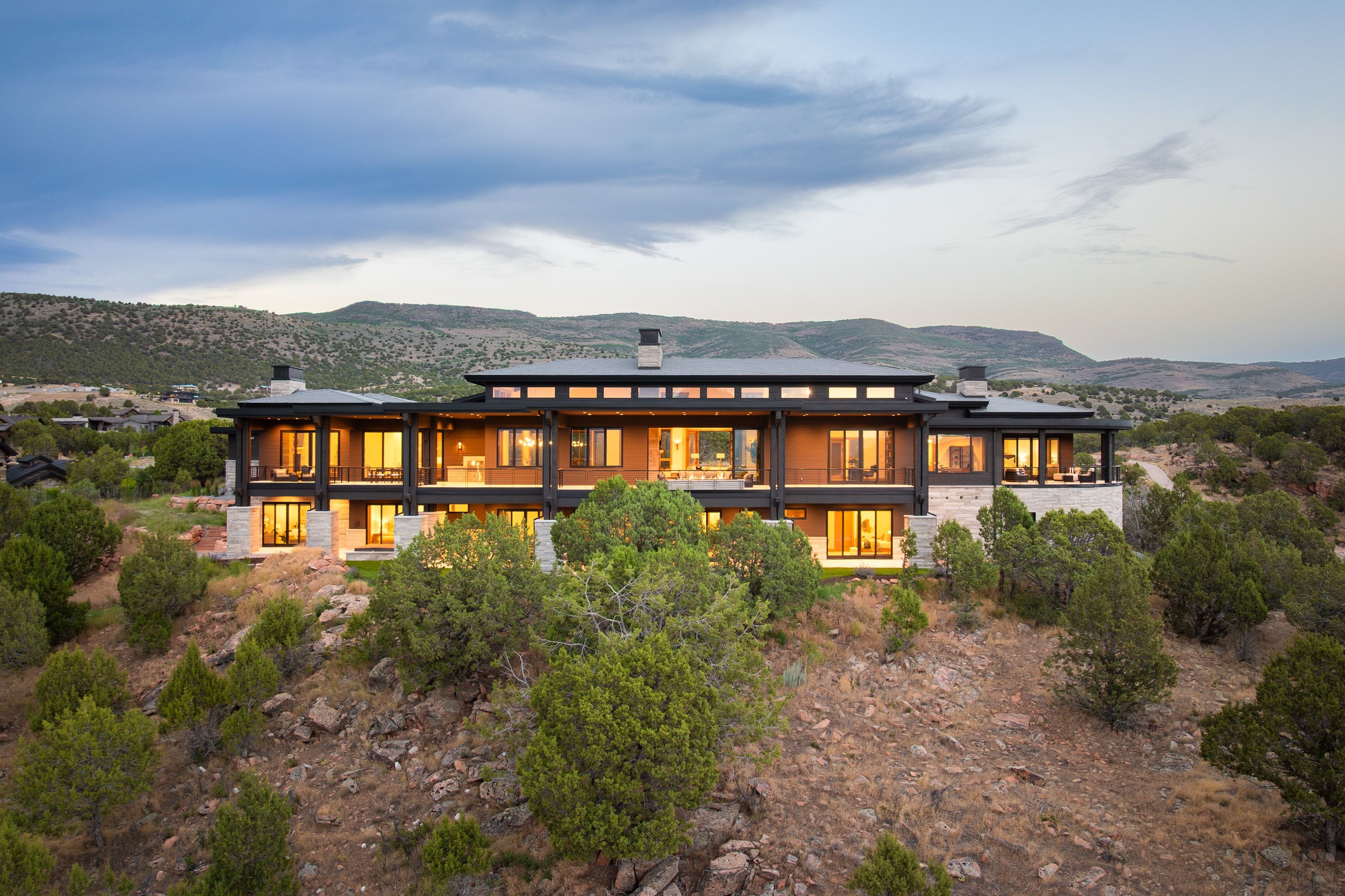 Contemporary architectural design with expansive window walls, multiple balconies, a stone and wood facade, and a flat roofline