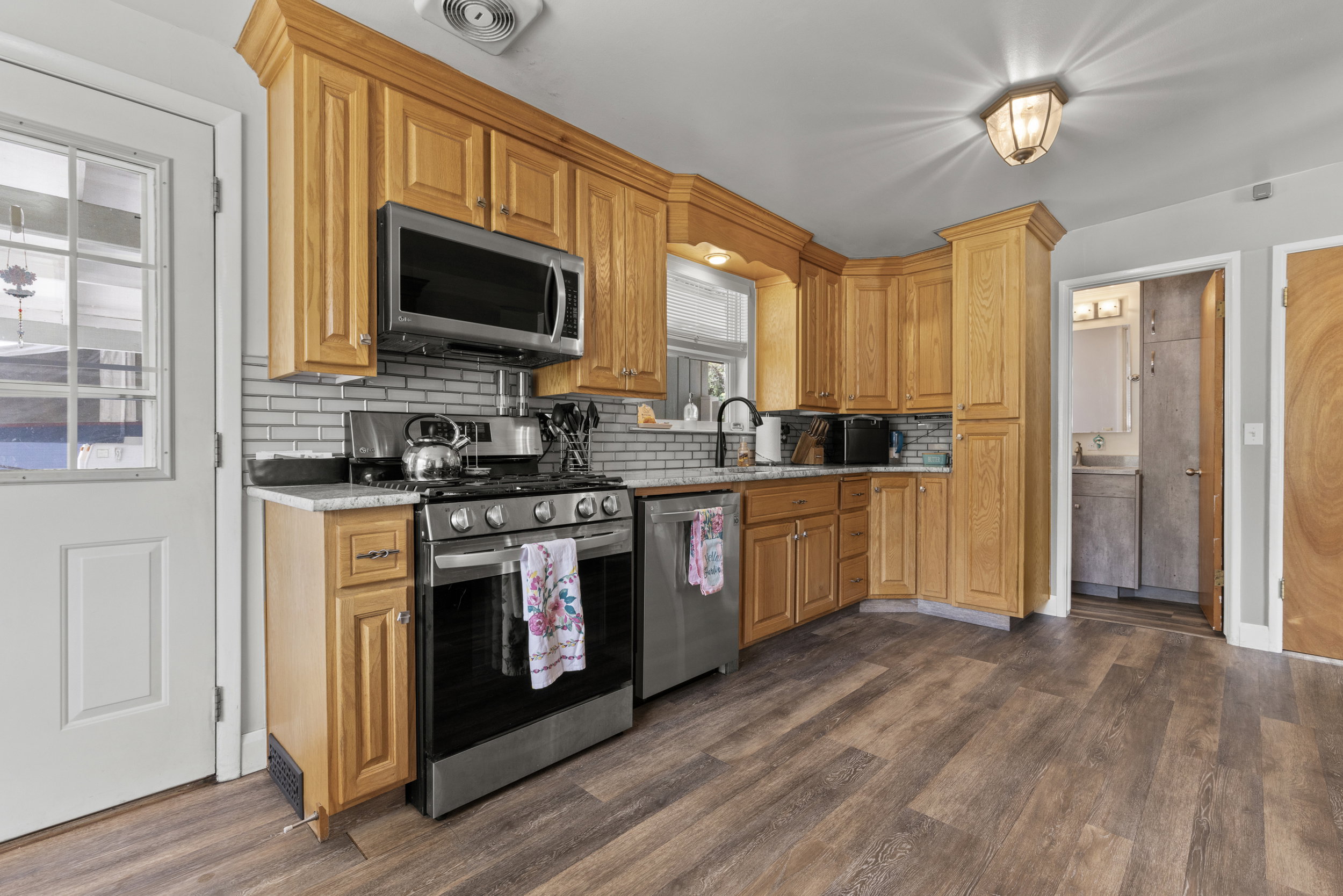 Kitchen featuring wood-finish flooring, light wood cabinetry, stainless steel appliances, a subway tile backsplash, and light-toned countertops