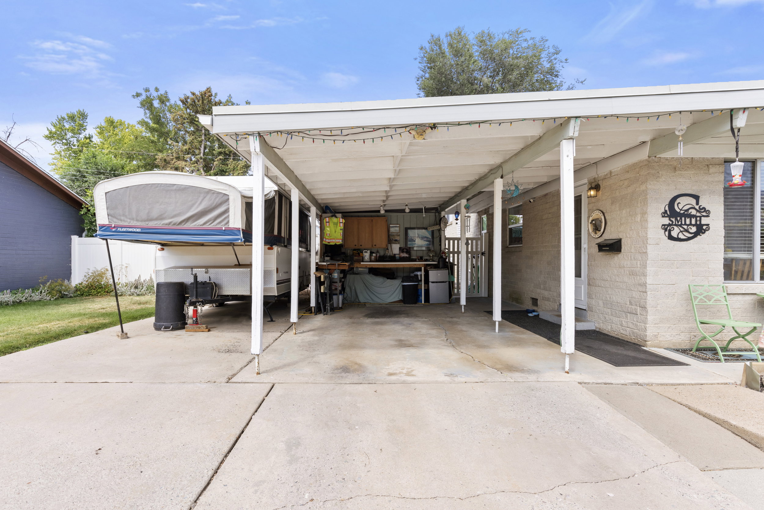 Covered carport featuring a concrete driveway, brick exterior, and white privacy fencing