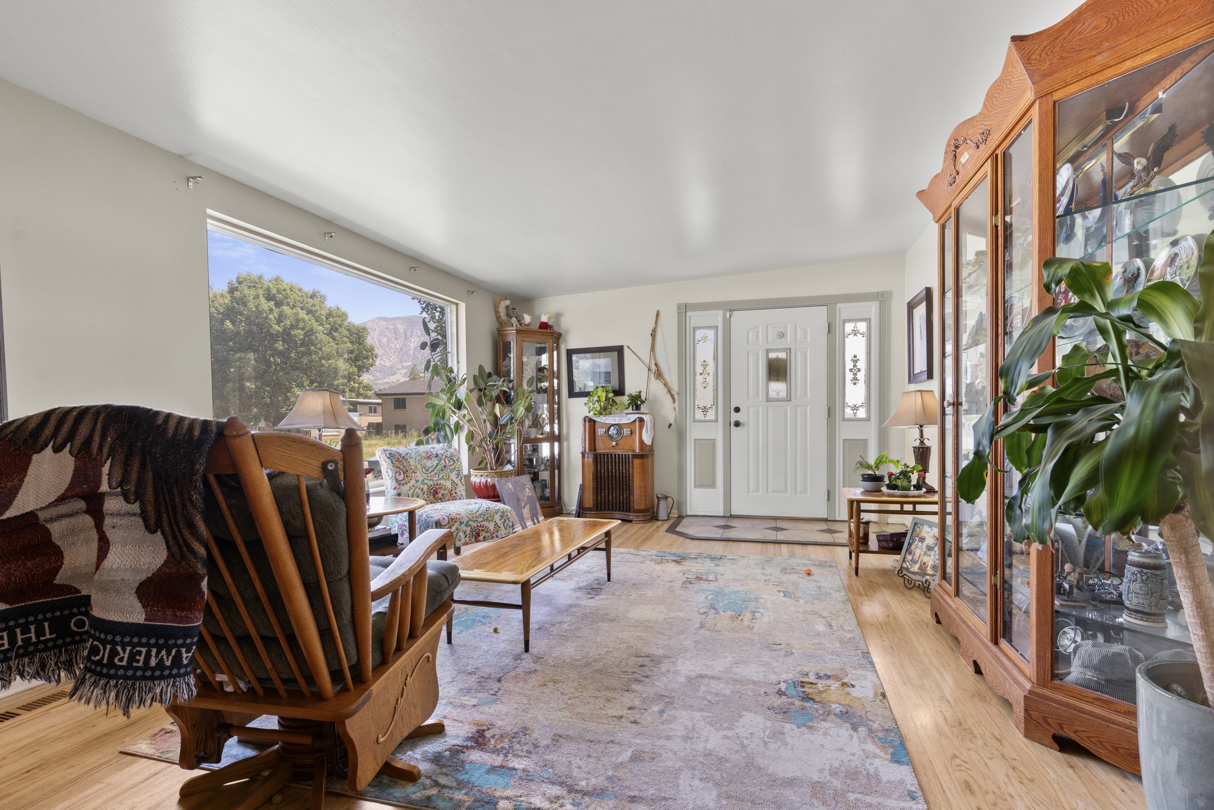 Expansive front room featuring wood-finish flooring, a broad front window, and a white entry door with decorative glass inserts and sidelights