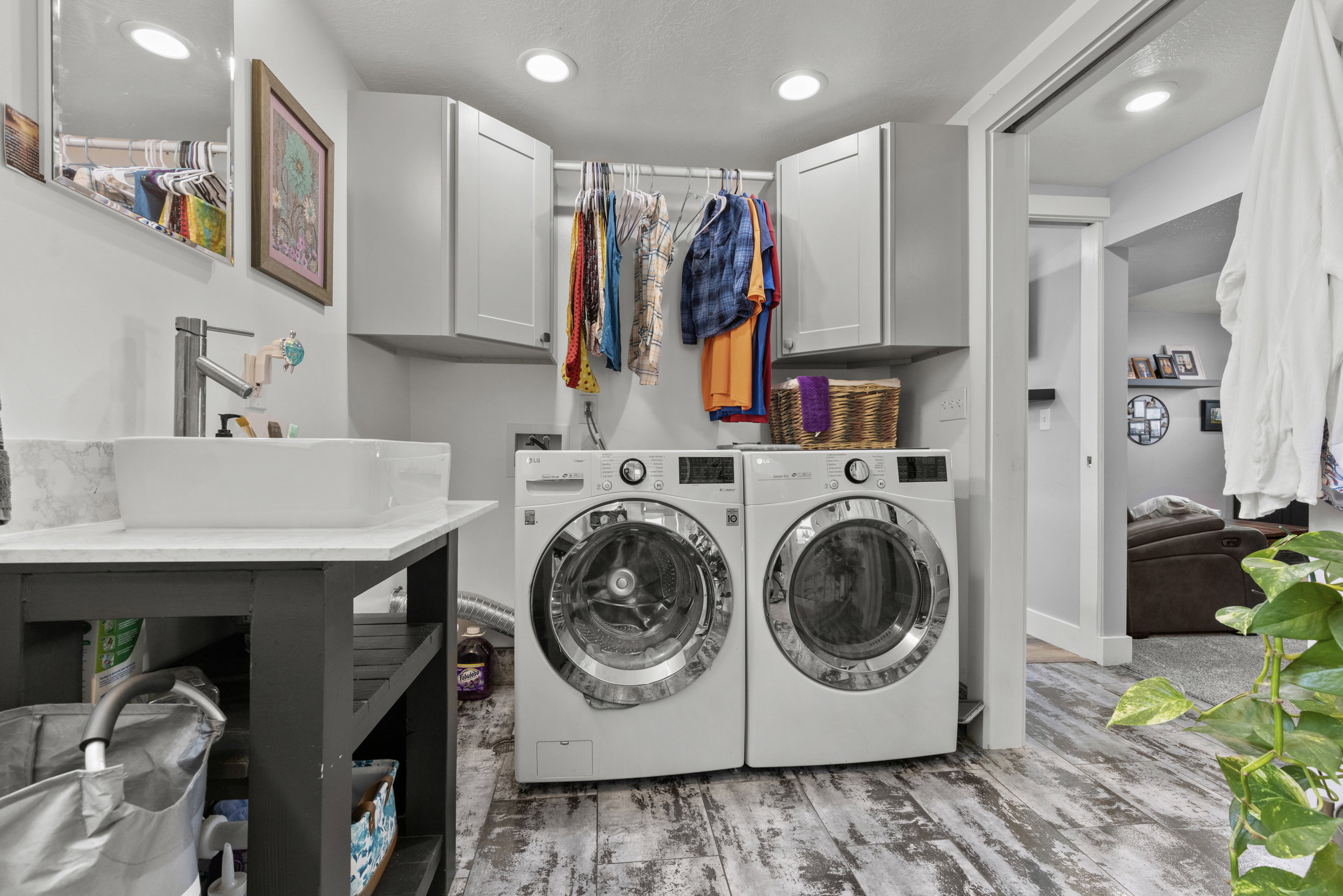 Dedicated laundry space featuring a vessel sink with a wall-mounted faucet, wood-finish flooring, two upper cabinets, and a built-in clothing rod