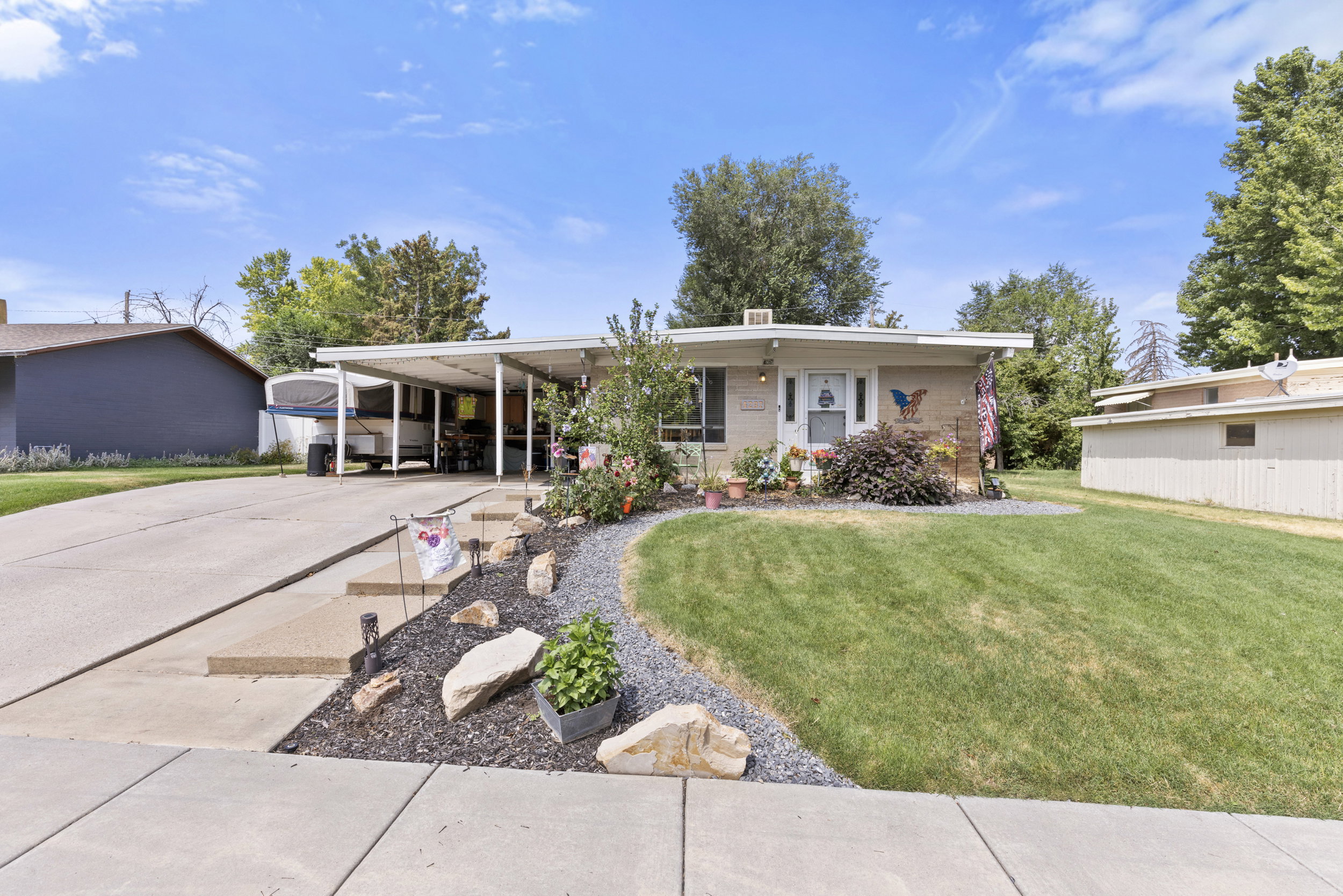 Single-level residence featuring a carport, front lawn, and established landscaping