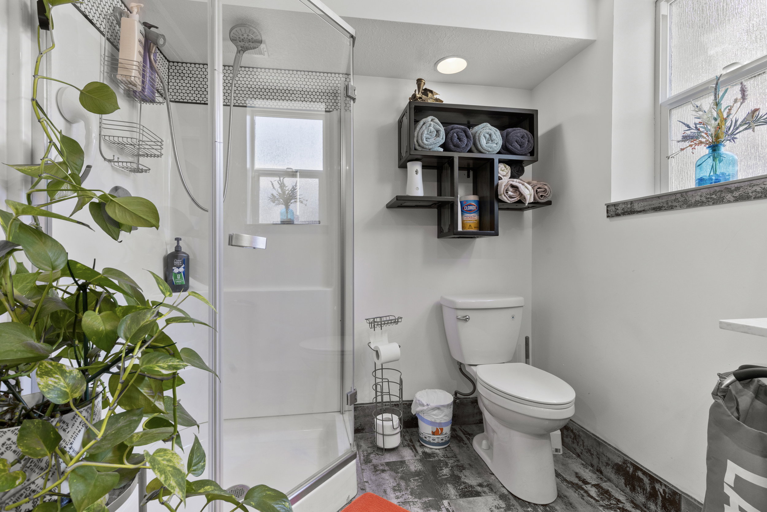 Bathroom featuring a glass-enclosed shower, built-in shelving, white toilet, window, and distressed wood-finish flooring