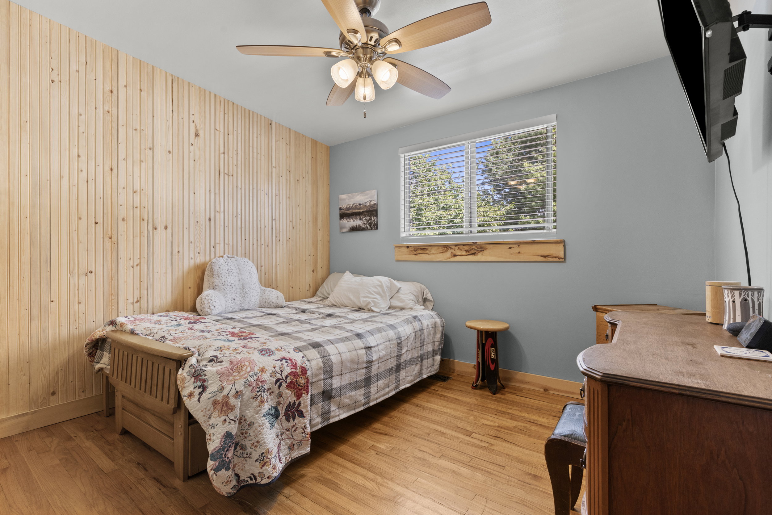 Bedroom featuring wood-finish flooring, a ceiling fan with integrated lighting, and a paneled accent wall
