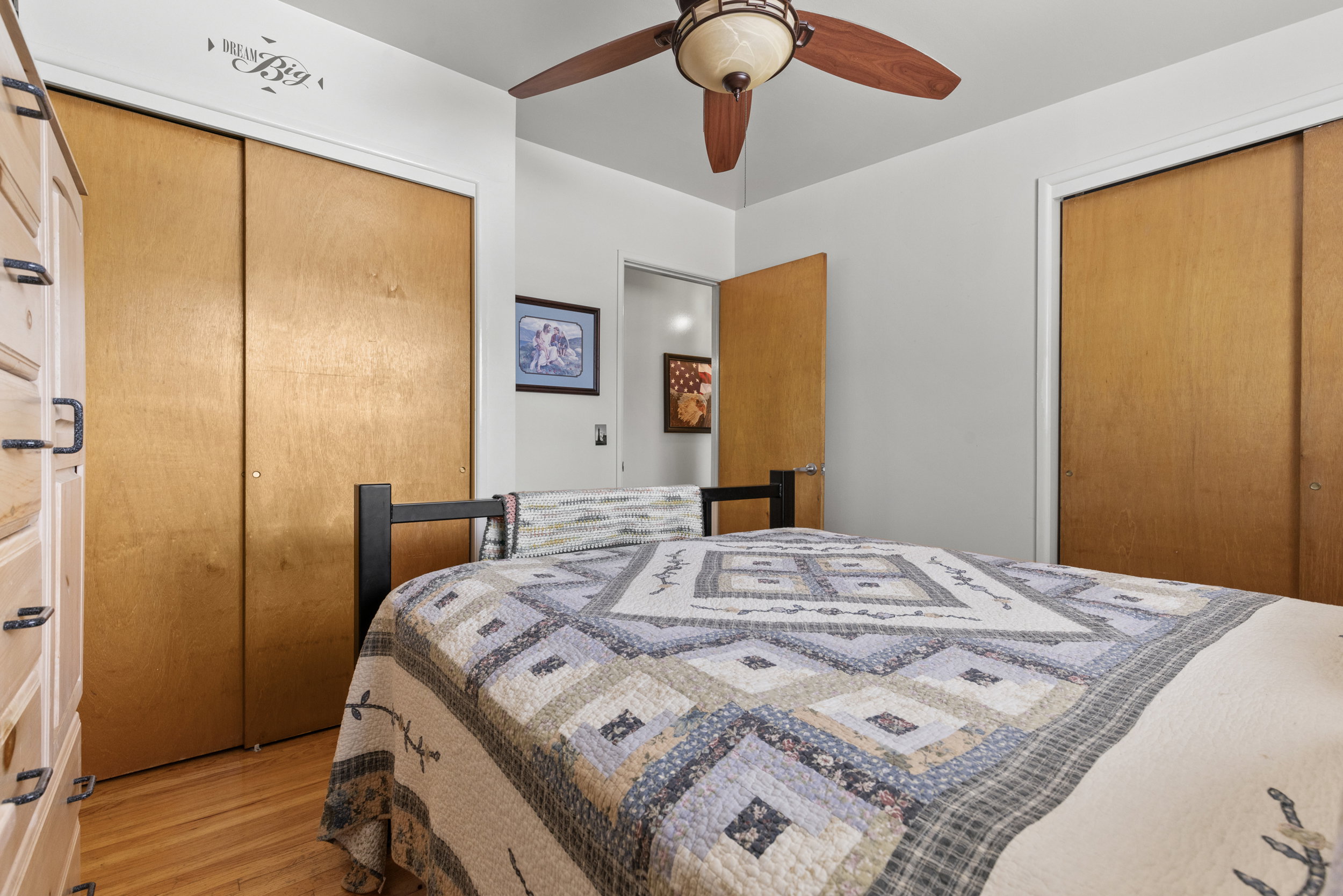 Bedroom featuring wood-finish flooring, two sets of bi-fold closet doors, and a ceiling fan with integrated lighting