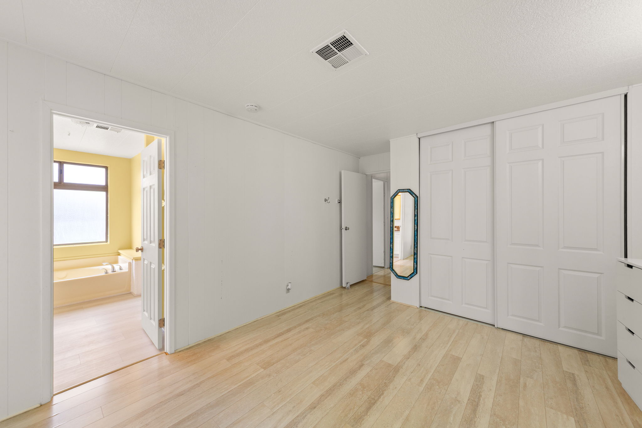 Bright room with light wood-finish flooring, white walls, and sliding panel closet doors