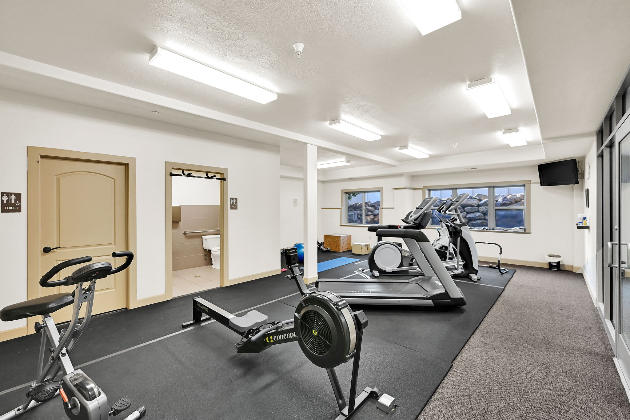 Gym on Level G: 10 Level (Ground) Fitness center featuring multiple exercise machines, bright overhead lighting, two bathrooms and durable rubber flooring