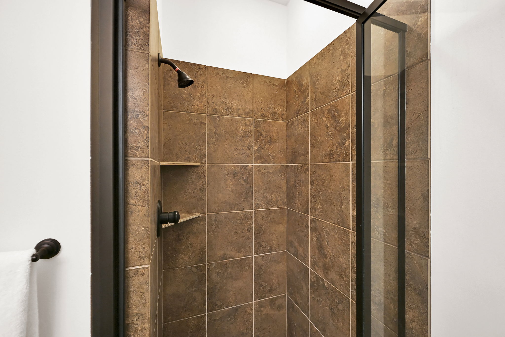 Shower enclosure featuring brown square-set wall tiles, a built-in shower niche, and oil-rubbed bronze fixtures