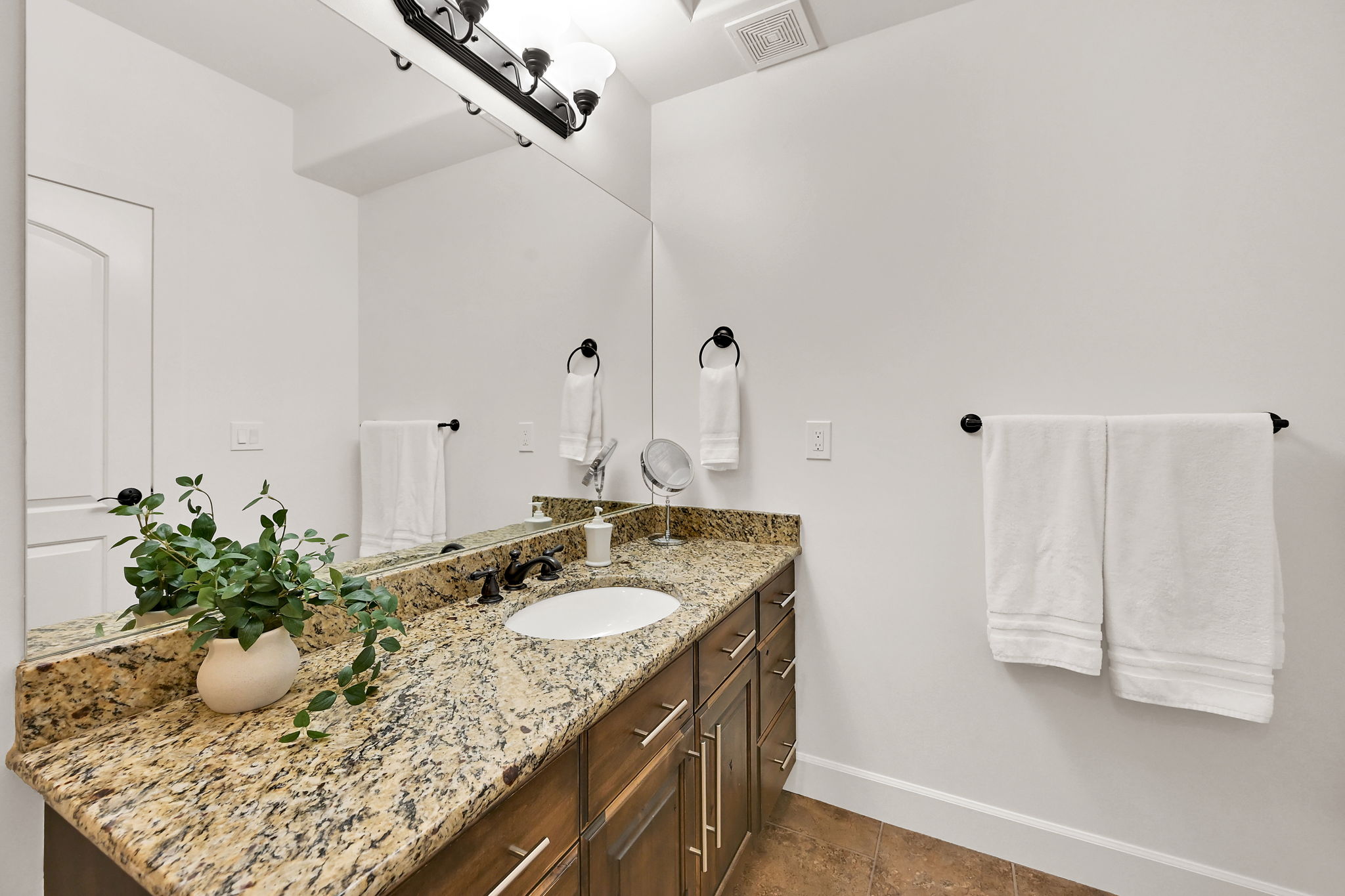 Primary Bathroom: Vanity featuring a granite countertop, undermount sink, dark bronze faucet, and wood-finish cabinetry with silver hardware