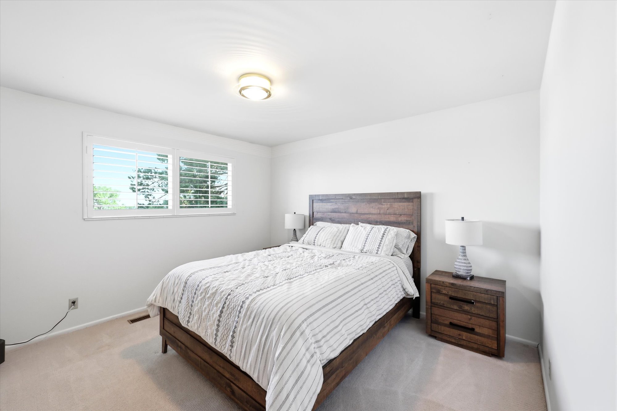 Bedroom featuring a double window with plantation shutters, light-colored carpeting, a contemporary ceiling light fixture, and white painted walls