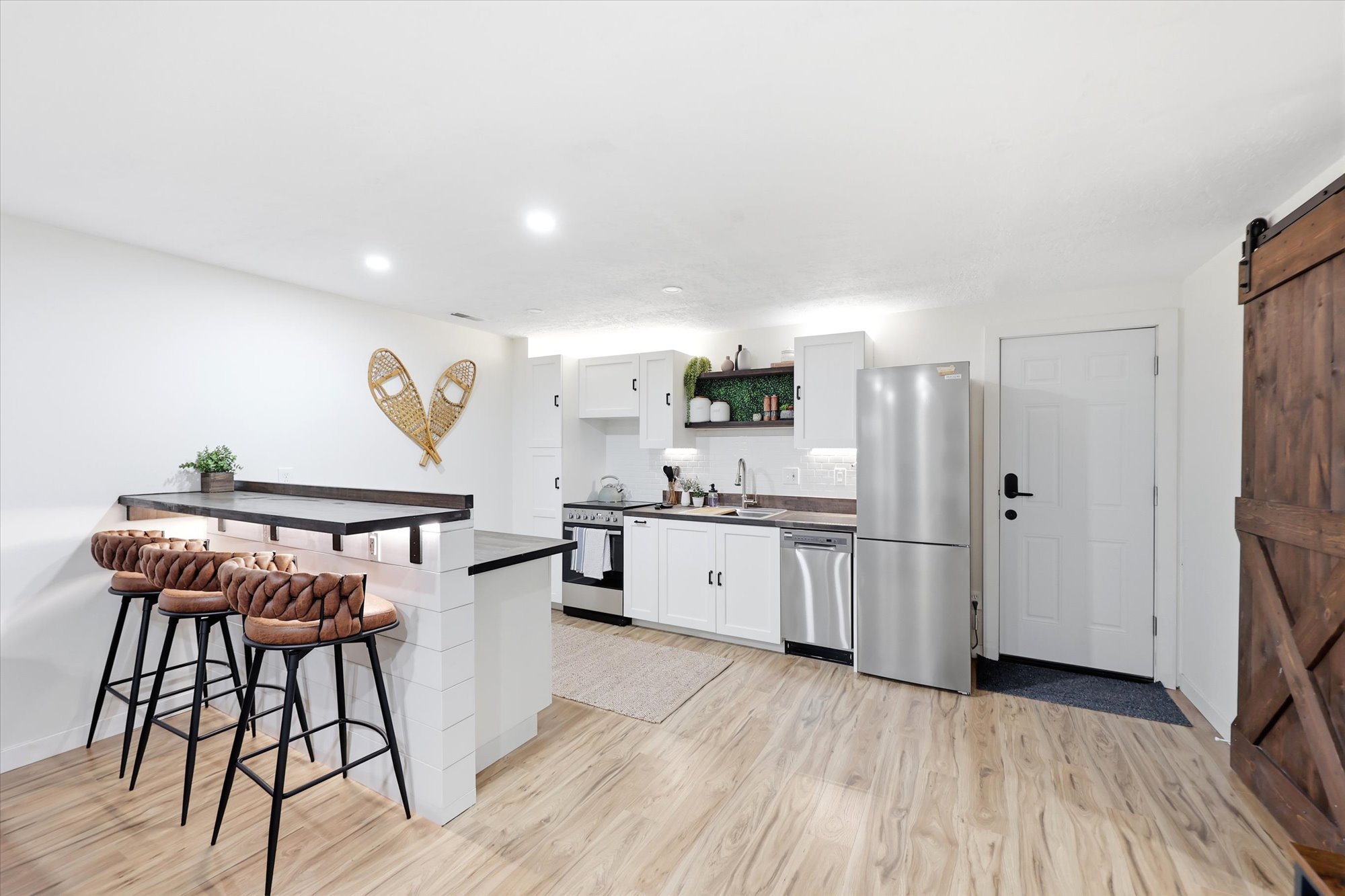 Open-concept kitchen featuring white cabinetry, stainless steel appliances, and a breakfast bar with dark countertops