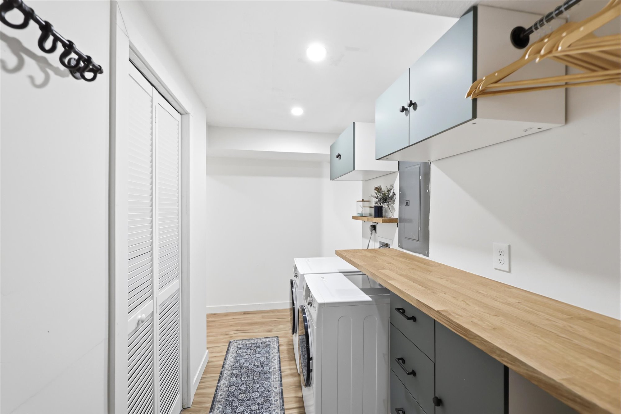 Laundry area featuring a wood-finish countertop, white cabinetry with black hardware, and louvered bi-fold doors