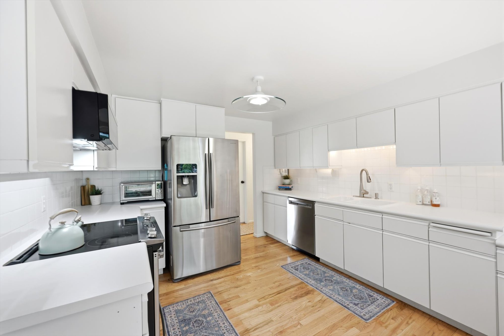 Modern kitchen featuring white cabinetry, light countertops, wood-finish flooring, stainless steel appliances, and a white subway tile backsplash