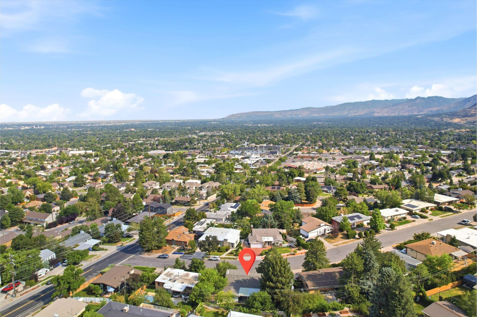 Expansive aerial view of a residential neighborhood with distant mountain backdrop, lush tree canopy, and well-established street grid