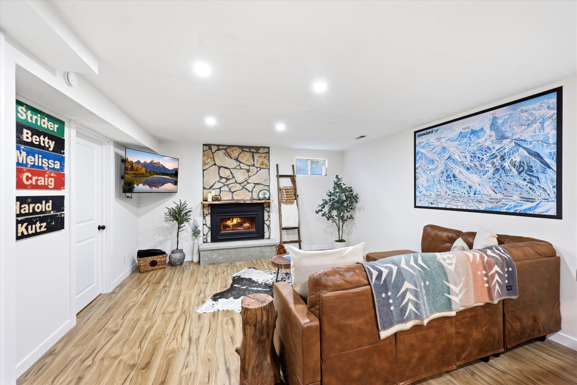 Spacious living area featuring light wood-finish flooring, a stone-clad fireplace with a hearth, recessed lighting, and white walls
