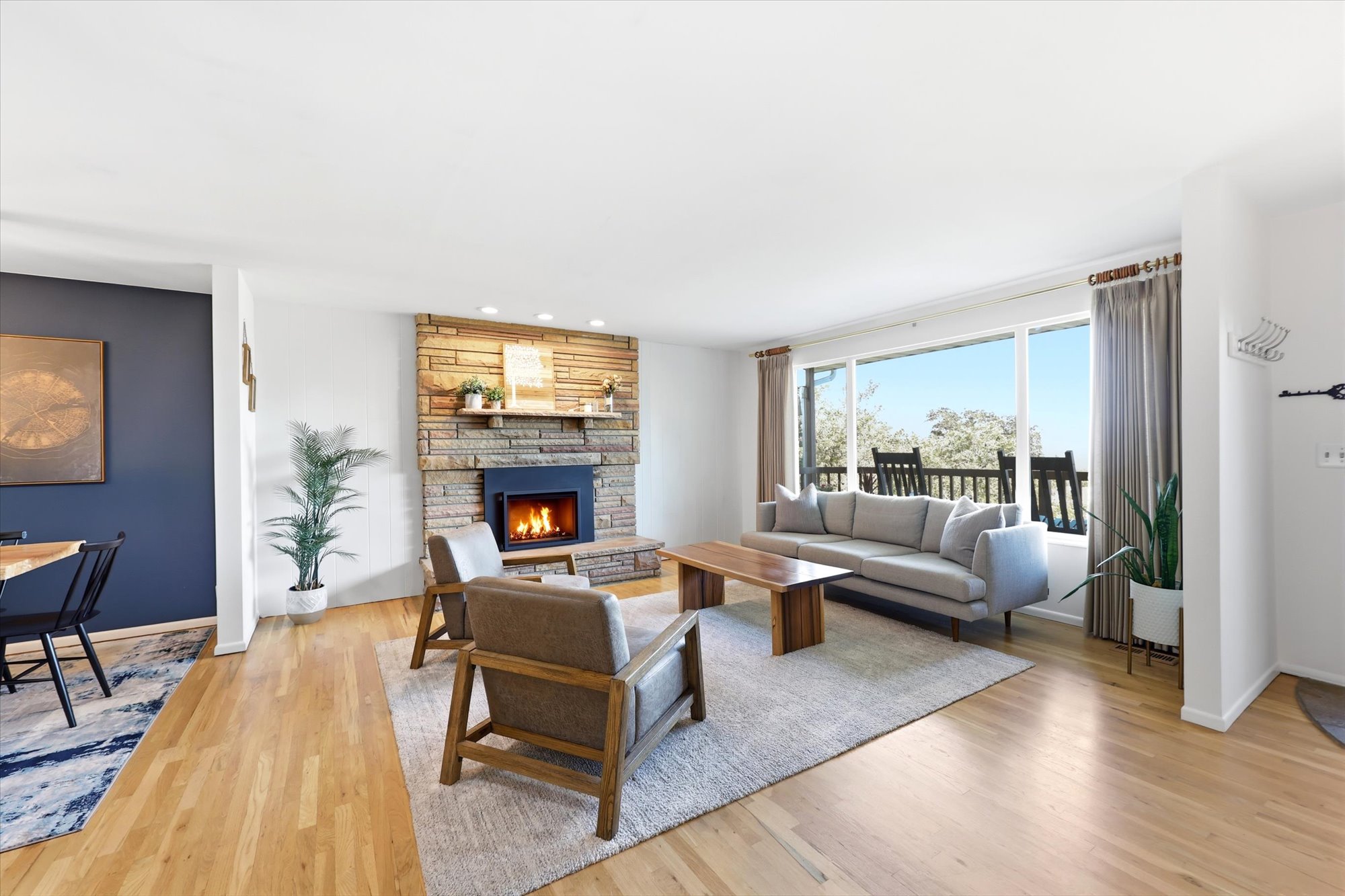 Living space featuring a stone fireplace, wood-finish flooring, recessed lighting, and large windows with outdoor access